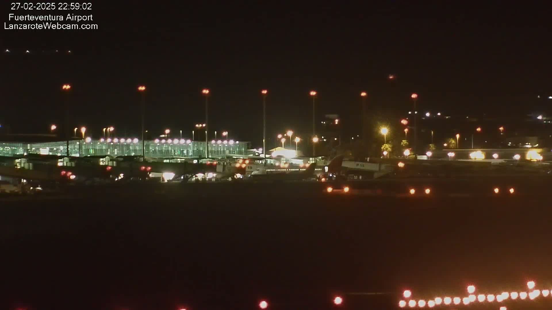 A brightly lit airport terminal and airplanes are visible at night.