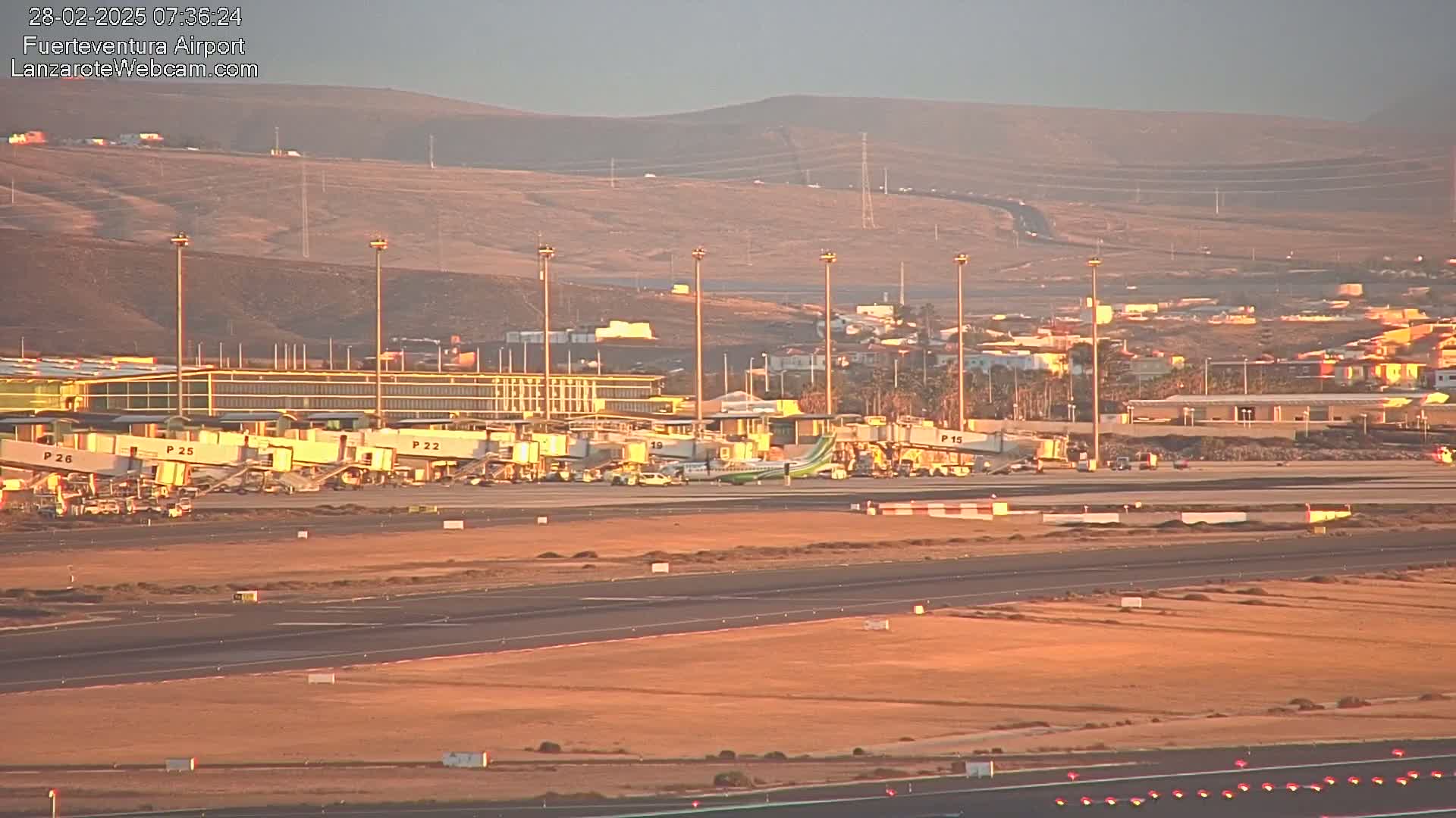 An airport with several planes at gates, jet bridges, and tarmac under a clear, light orange sunset sky.