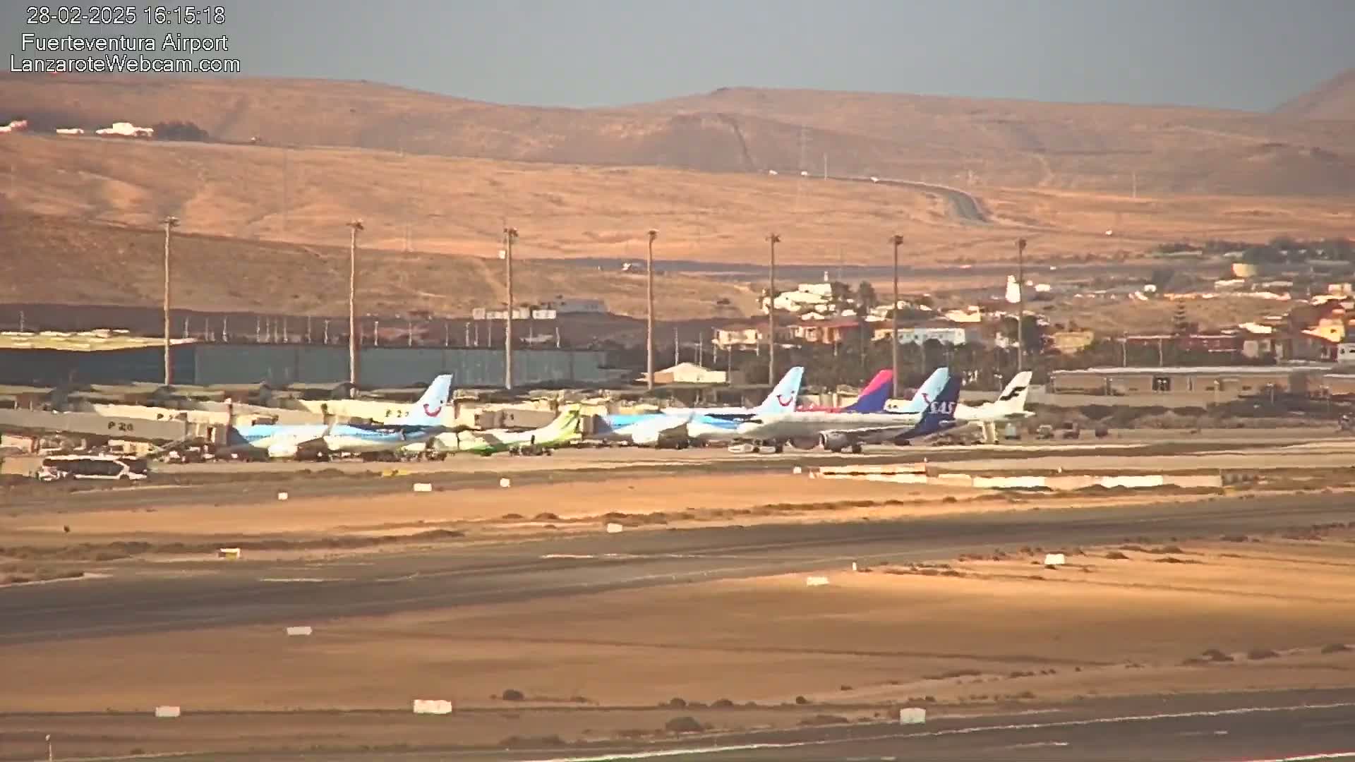Several airplanes are parked on a tarmac at an airport, under hazy or dusty outdoor conditions with a tan-colored landscape in the background.
