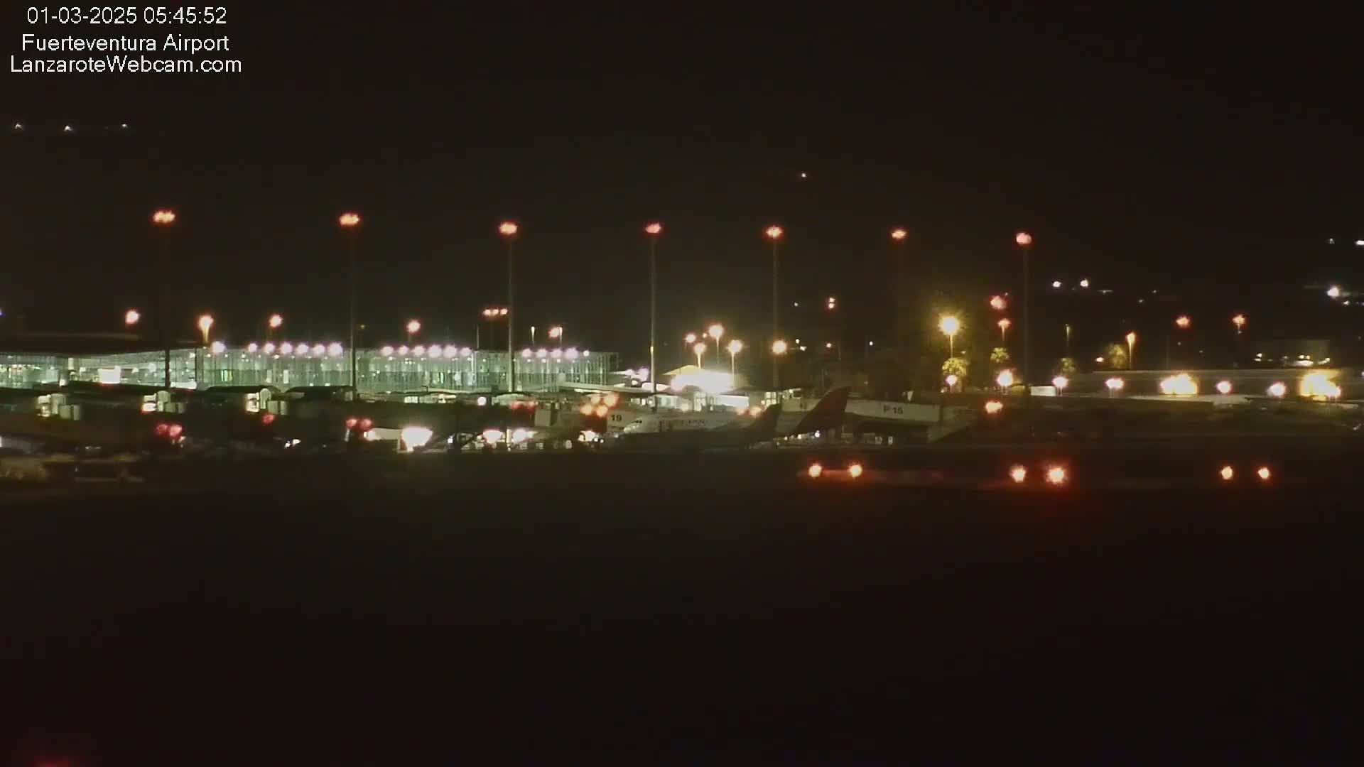 At night, several airplanes are parked near a brightly lit airport terminal under a clear, dark sky.