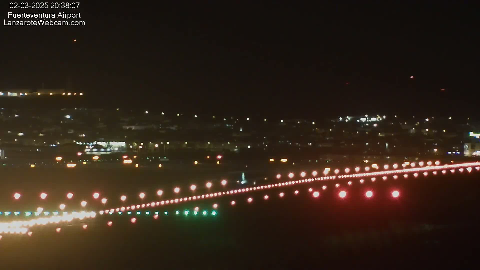 A nighttime view of a city with airport runway lights illuminating a landing strip.