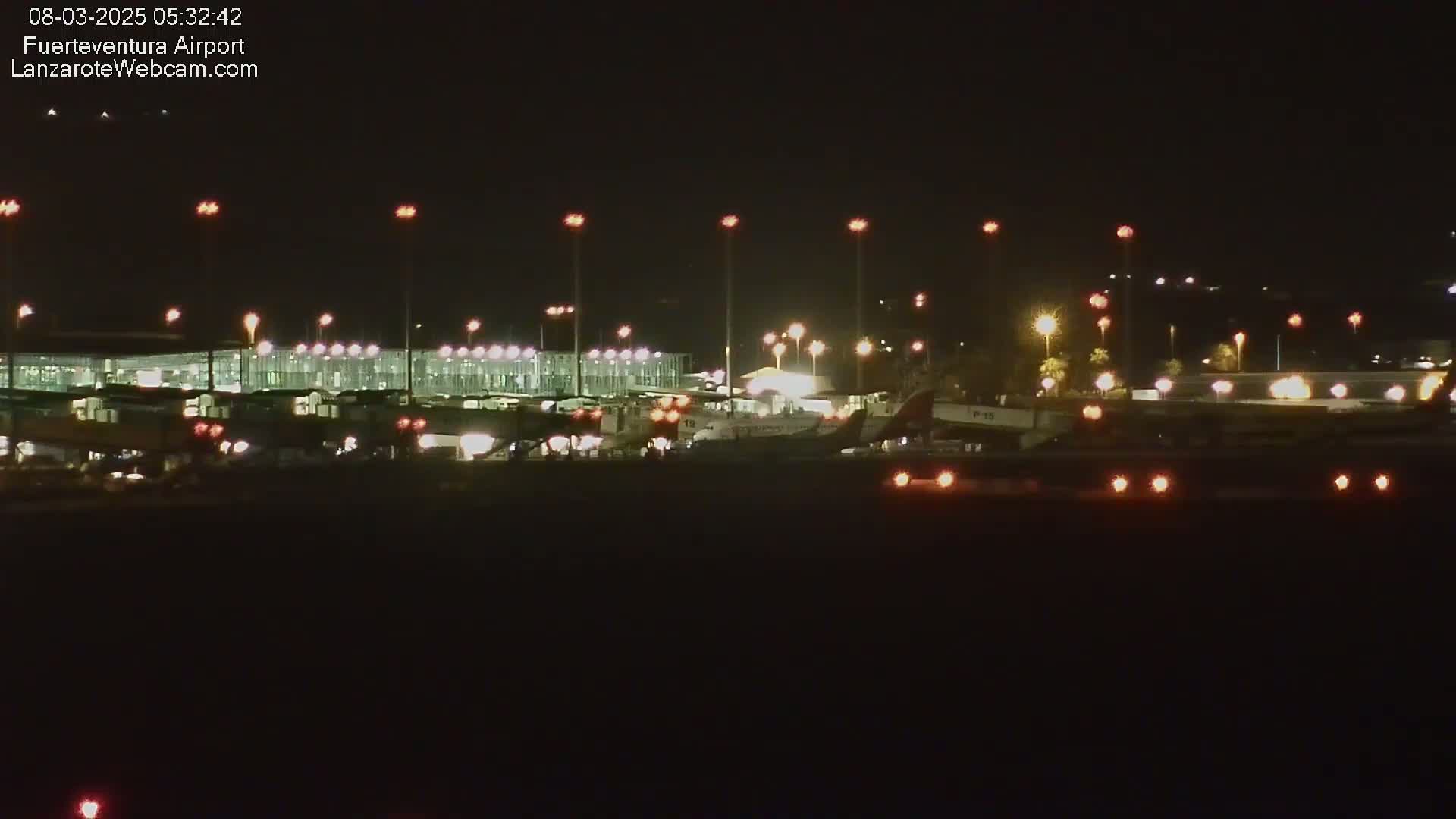 At night, several airplanes are parked at a brightly lit airport.