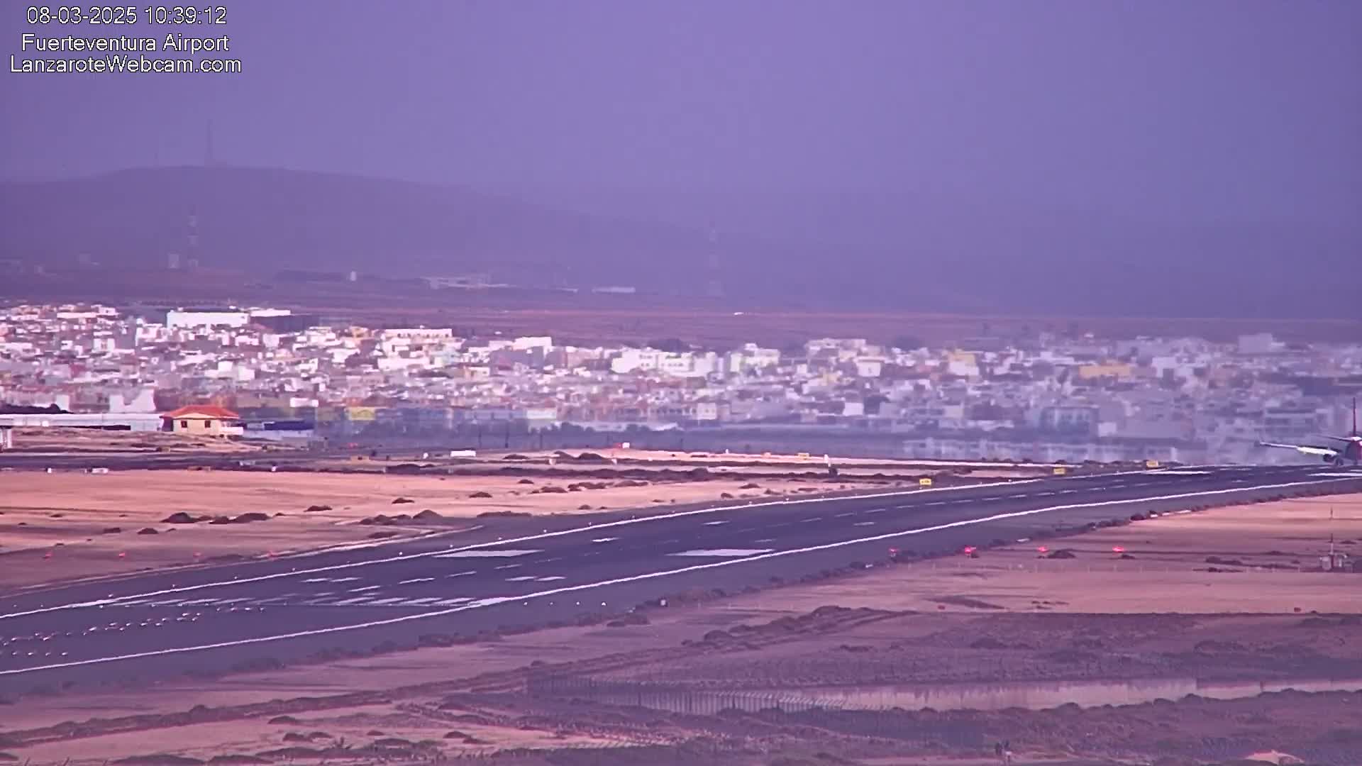 An airplane lands on a runway at an airport near a town under hazy conditions.