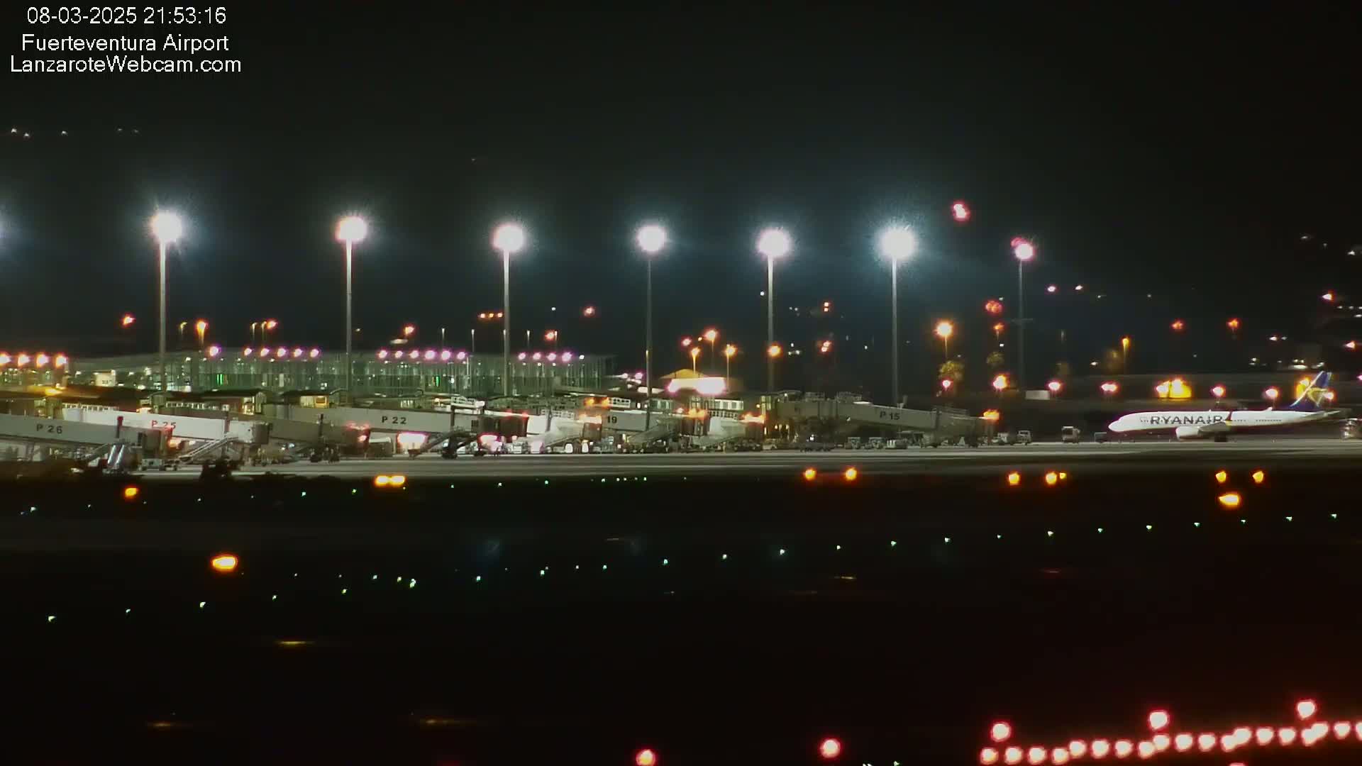 A Ryanair airplane is parked at a brightly lit airport at night.
