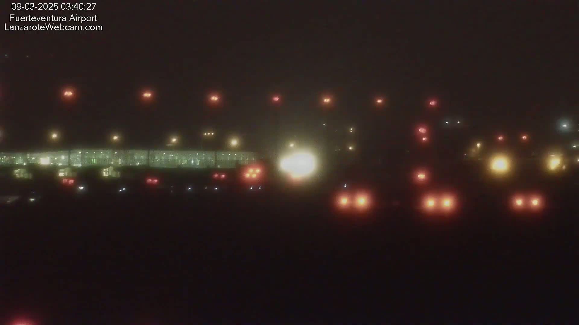 A nighttime, foggy view of an airport runway with various lights visible on the ground and in the distance.