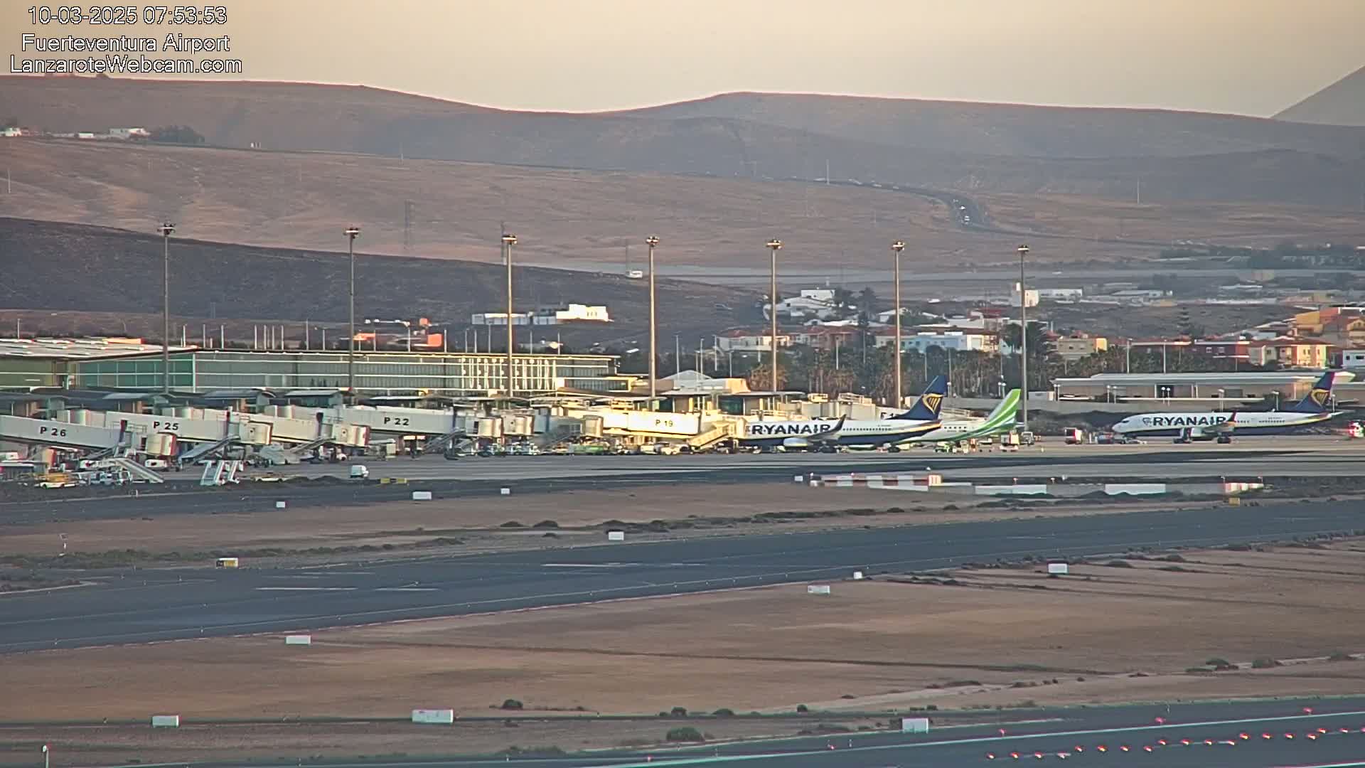 An airport tarmac with several airplanes and jet bridges, under a clear, dusky sky with distant hills.