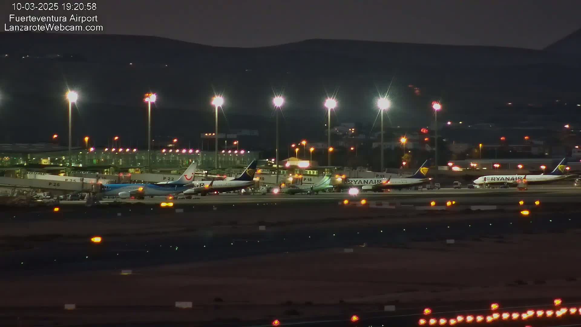 Several airplanes are parked at a brightly lit airport at night under a dark sky.