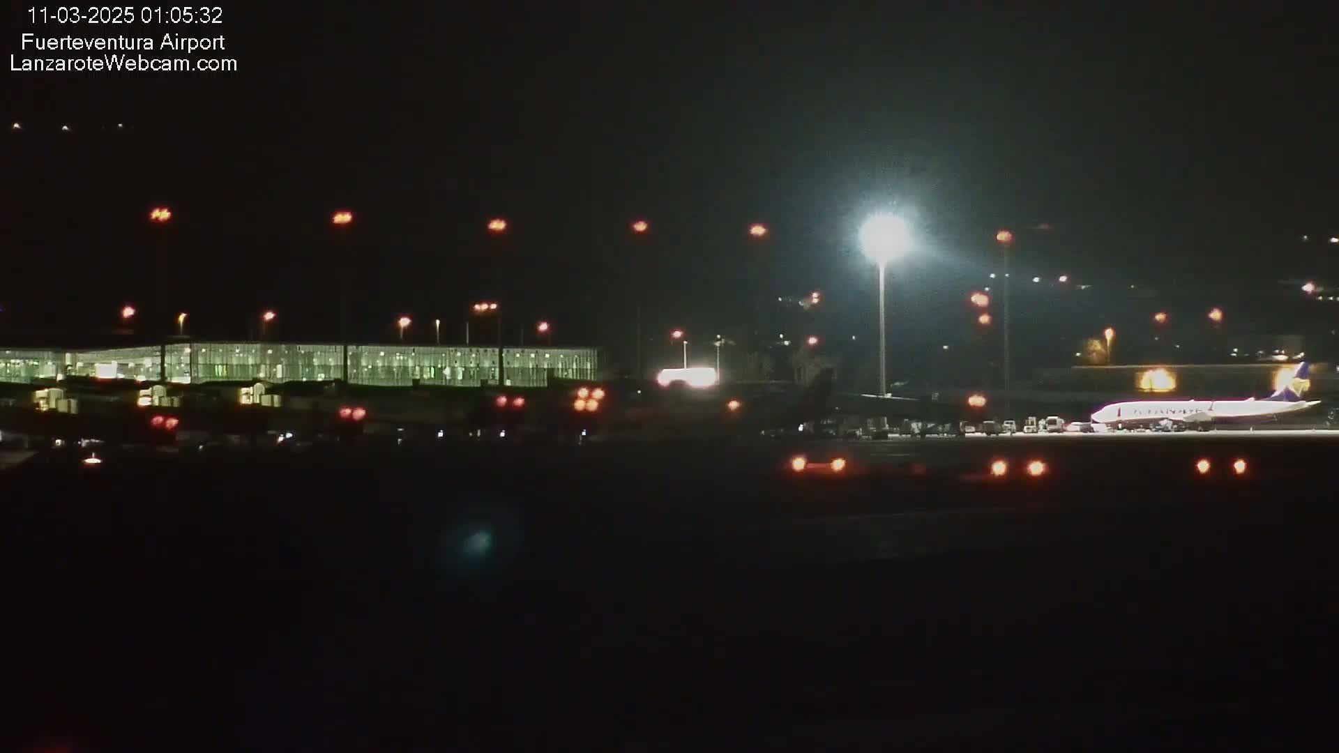 At night, a large airplane sits on the tarmac of an airport with several lights illuminating the area.
