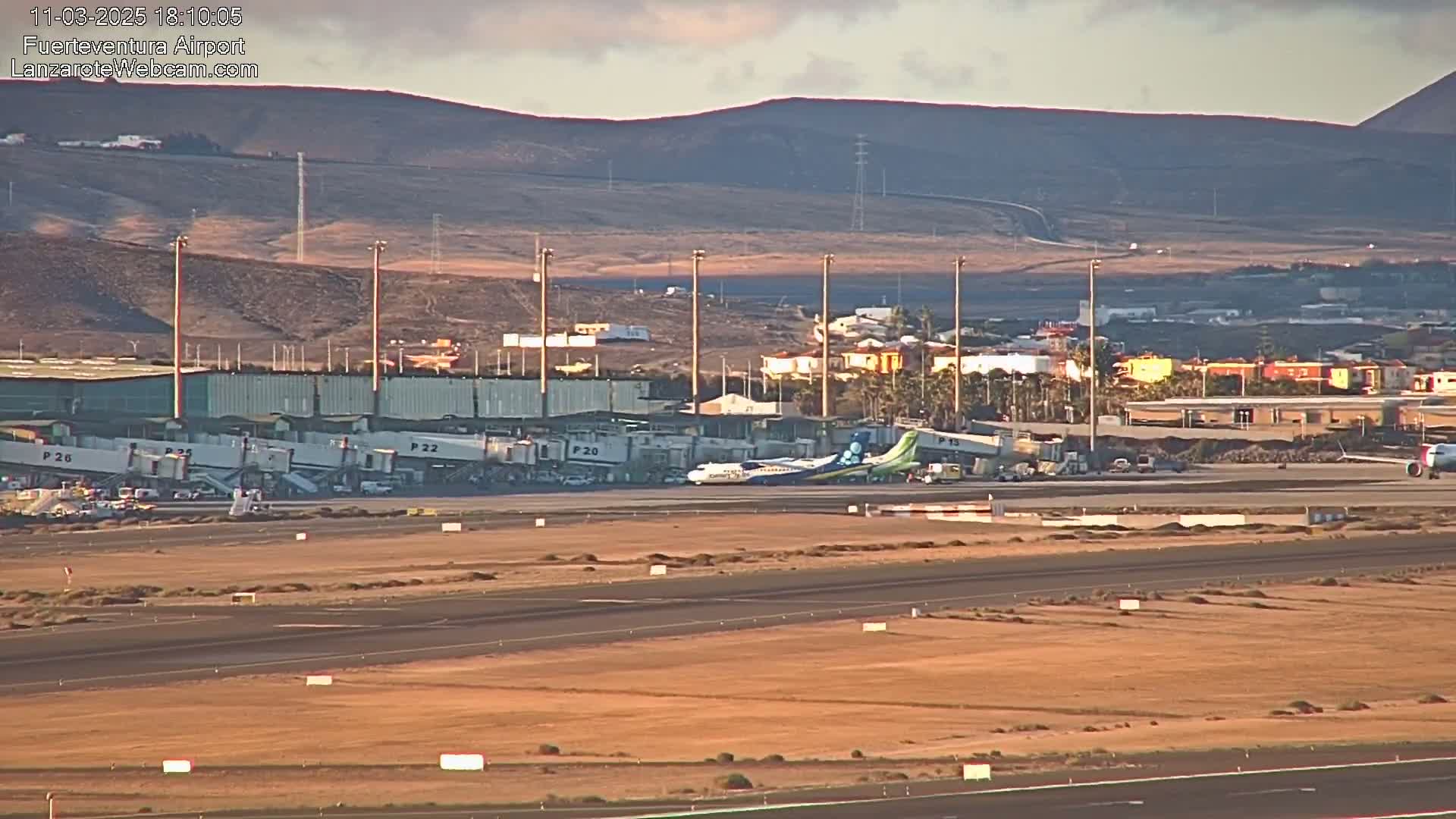 A turboprop airplane is parked at a gate of an airport, with buildings and a runway visible under a clear sky.