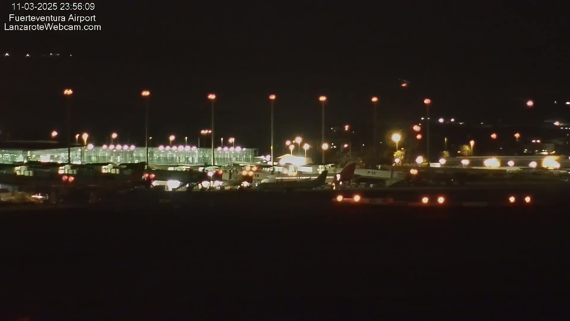 A nighttime view of an airport with several airplanes parked at gates, illuminated by numerous lights.