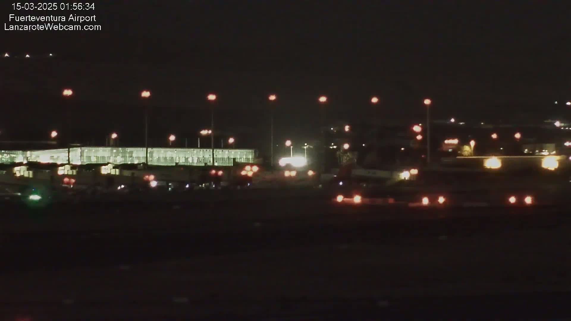 A nighttime view of an airport tarmac with several vehicles and a large illuminated building in the background.