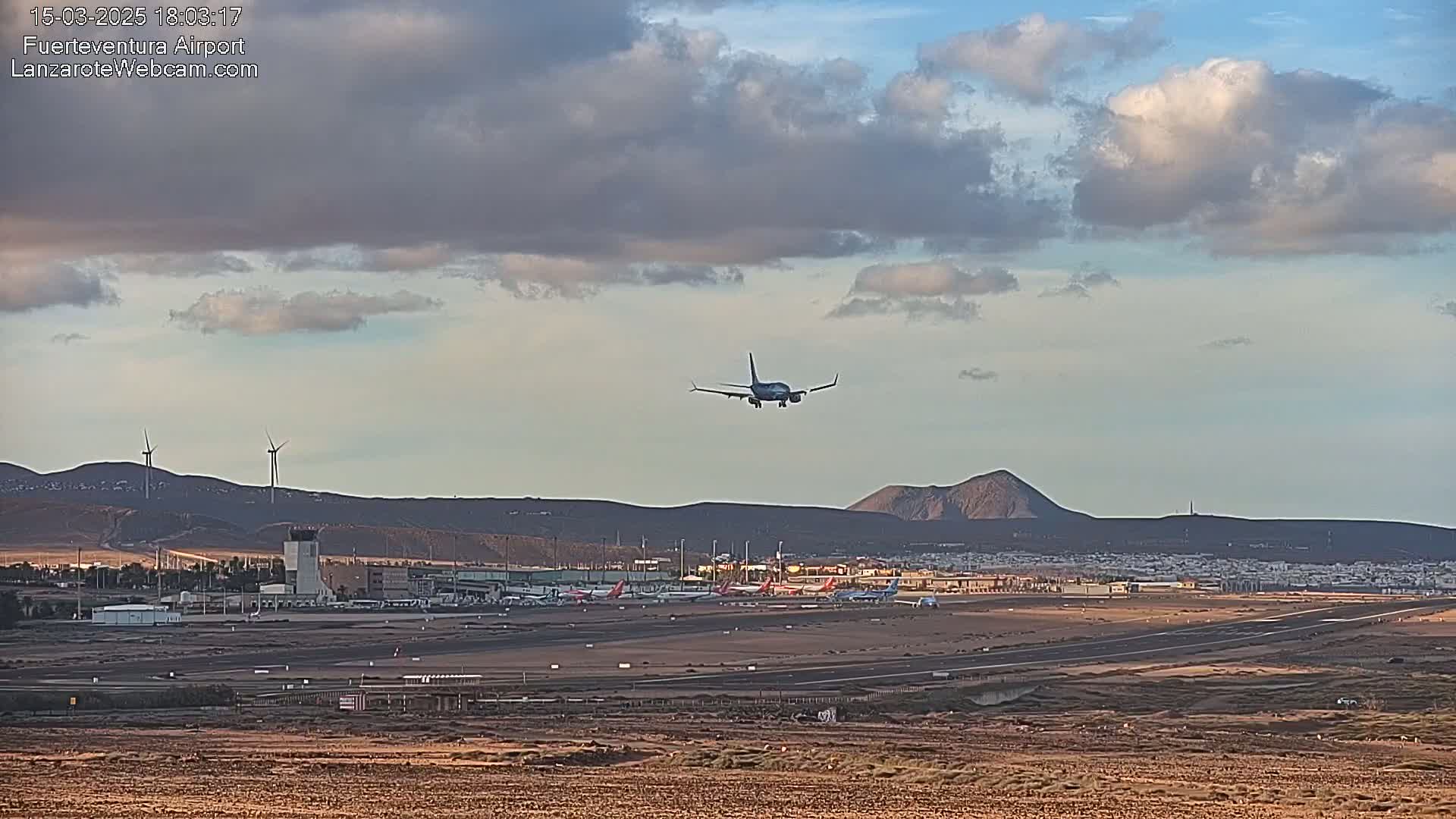 A passenger plane is descending toward an airport runway under a partly cloudy sky.