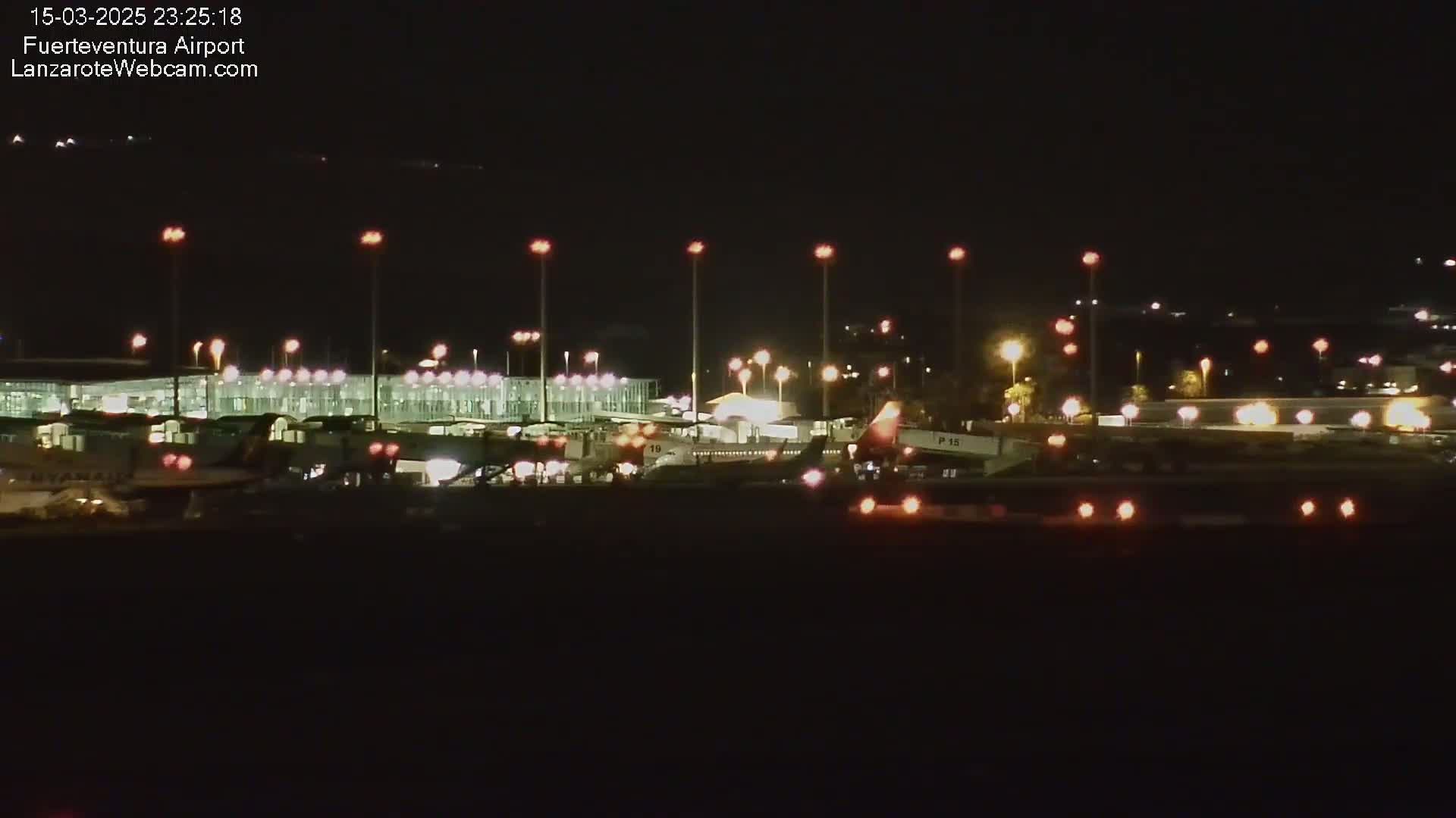 At night, airplanes are parked at gates of a brightly lit airport terminal under a clear, dark sky.