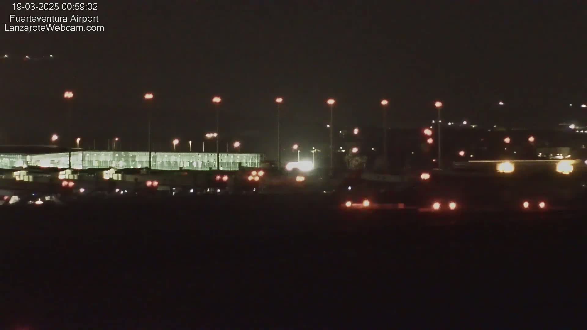 A nighttime view of an airport terminal building and surrounding area, illuminated by numerous lights, under a dark sky.
