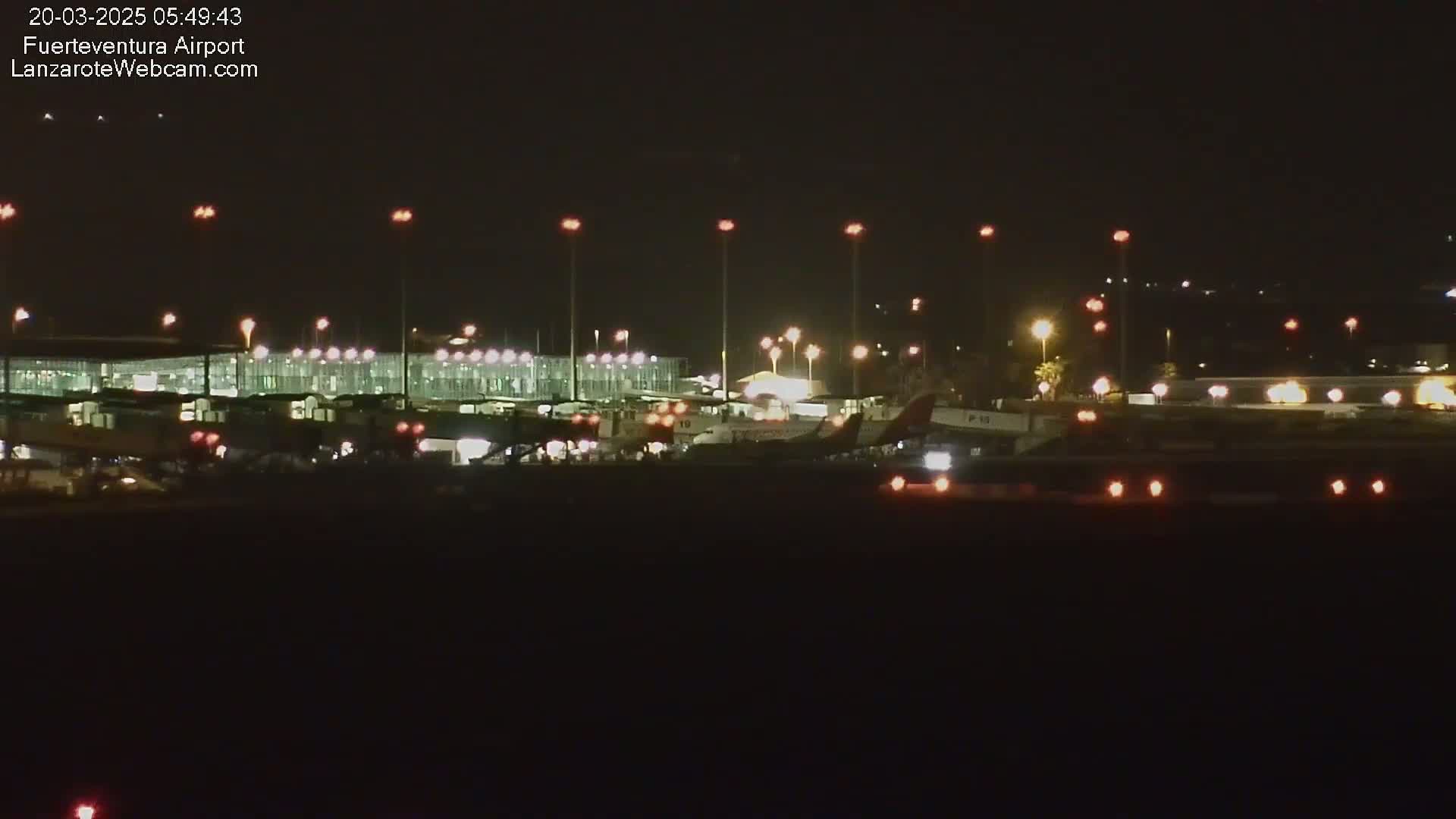 At night, several airplanes are parked at a brightly lit airport terminal under a clear, dark sky.