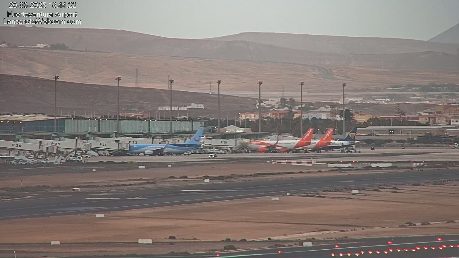 Several airplanes are parked at gates at an airport in front of a terminal building, under an overcast sky.