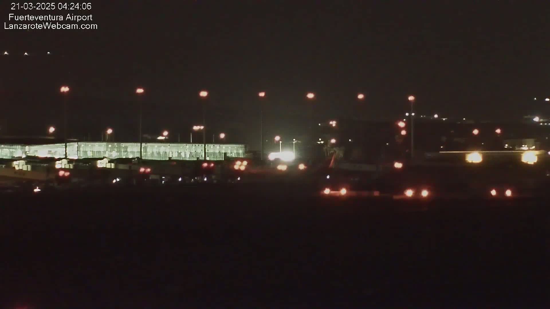 A long, brightly lit building is visible at night, with numerous vehicles and lights scattered in the foreground and background.