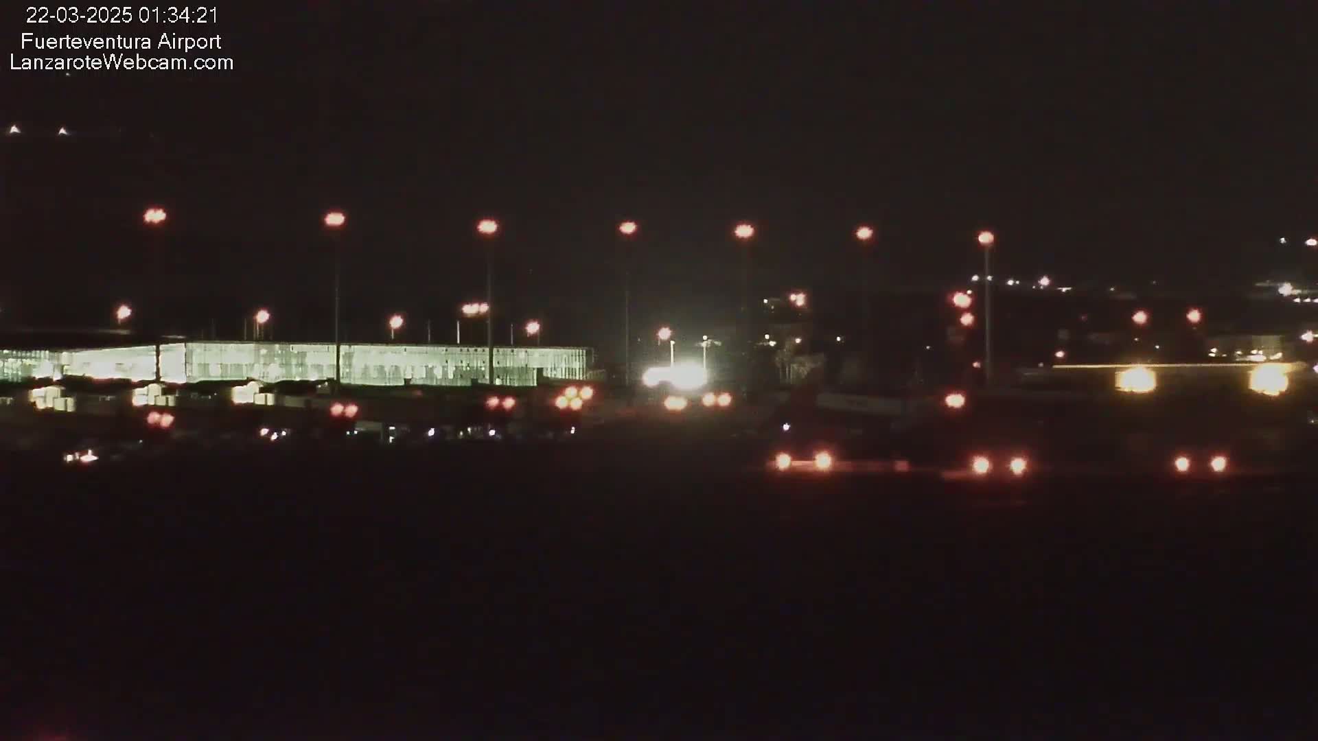 A brightly lit airport terminal at night is visible under a dark sky.