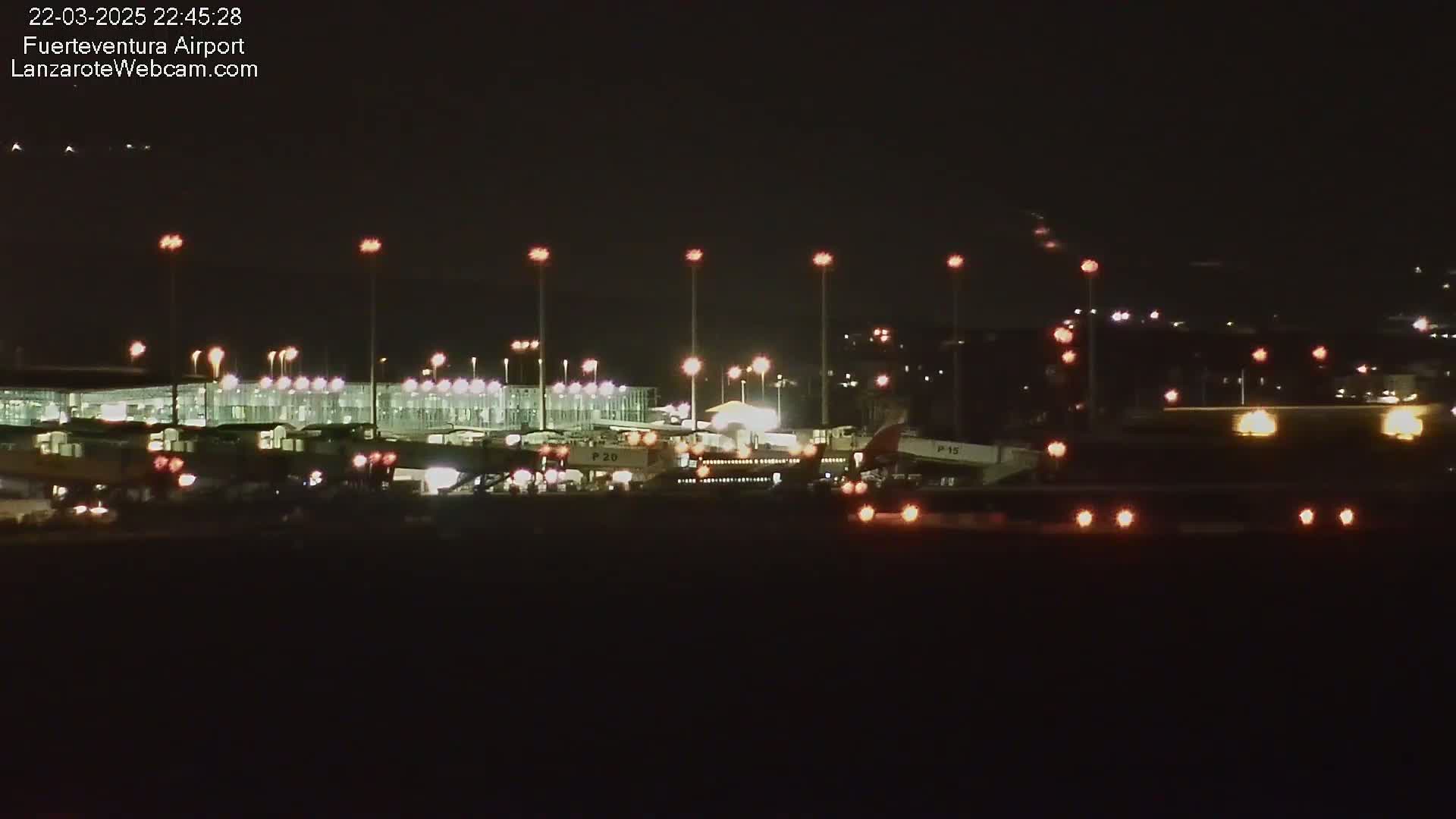 At night, a brightly lit airport terminal and several airplanes are visible on the tarmac, under a clear, dark sky.
