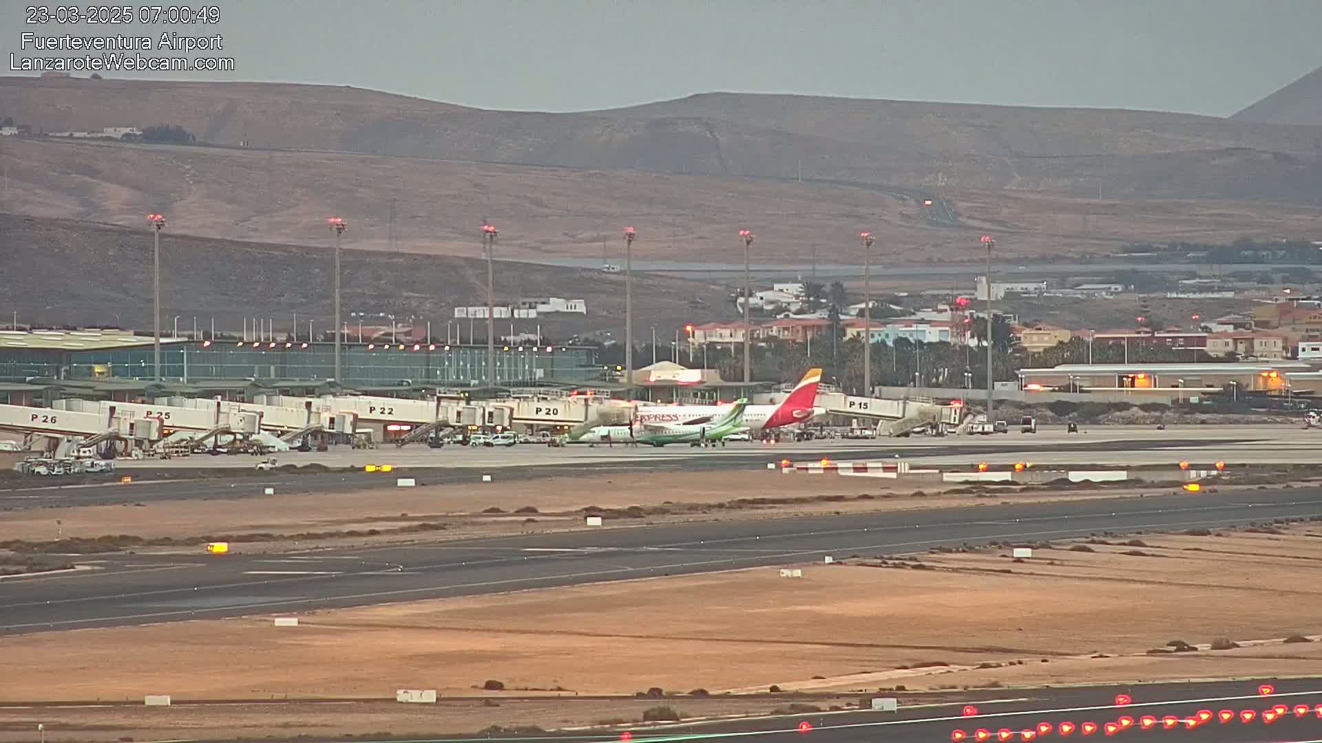 An airplane is parked at a gate at an airport, under a mostly clear, dusky sky, with several other planes visible at nearby gates.