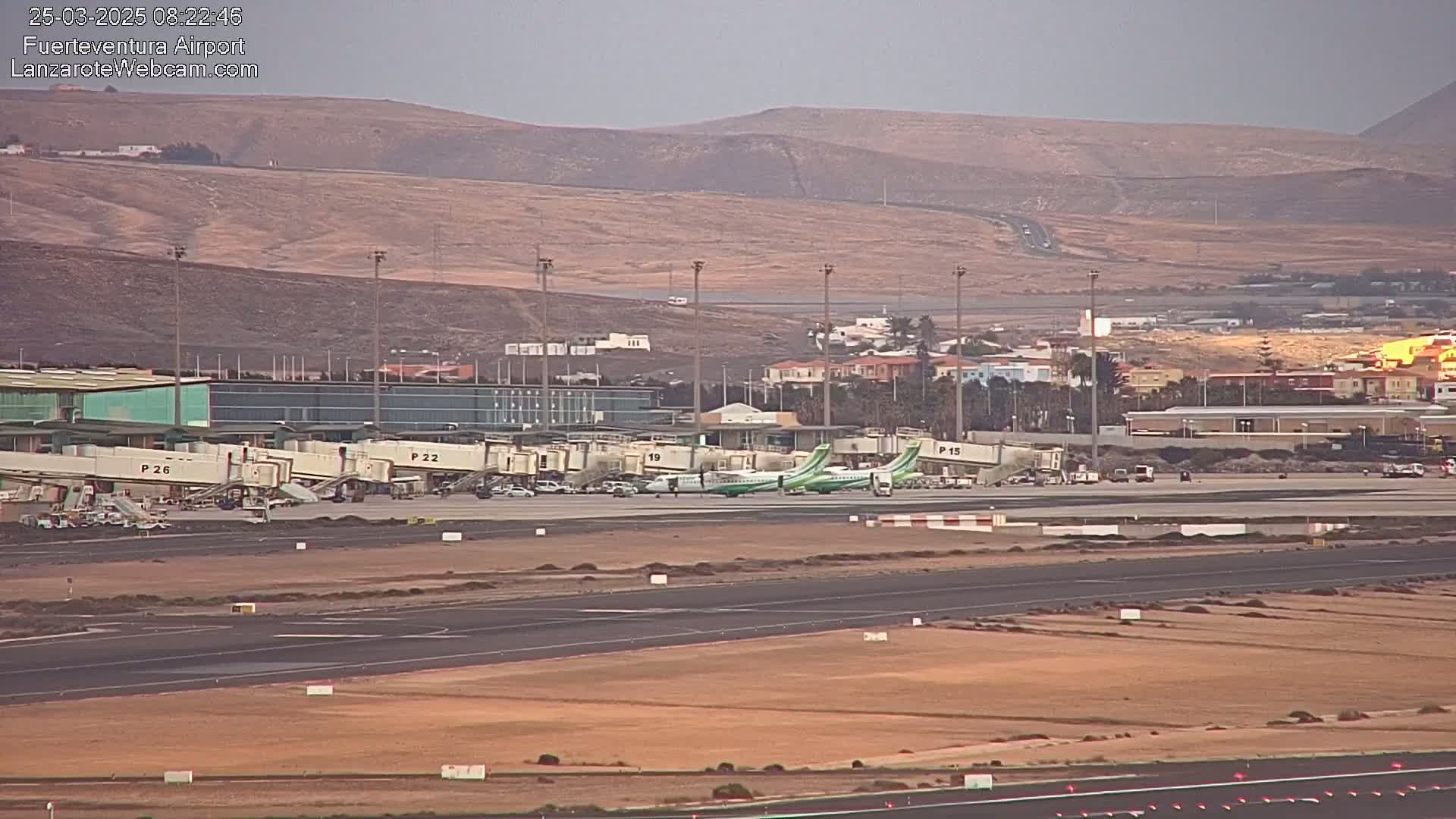 An airport tarmac with several airplanes parked at gates, jet bridges, and surrounding buildings under a hazy sky.