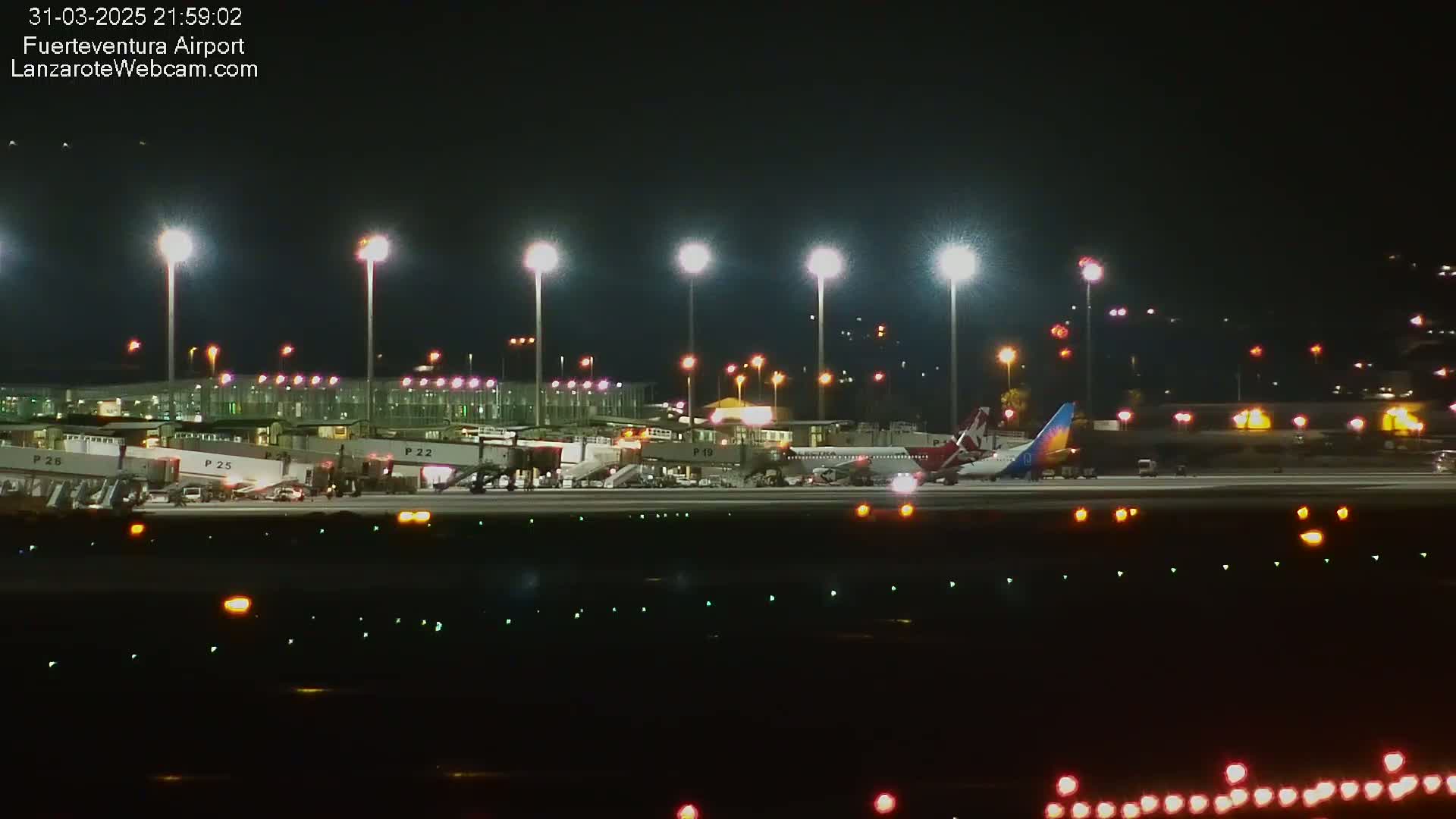 At night, brightly lit airplanes are parked at gates at an airport.