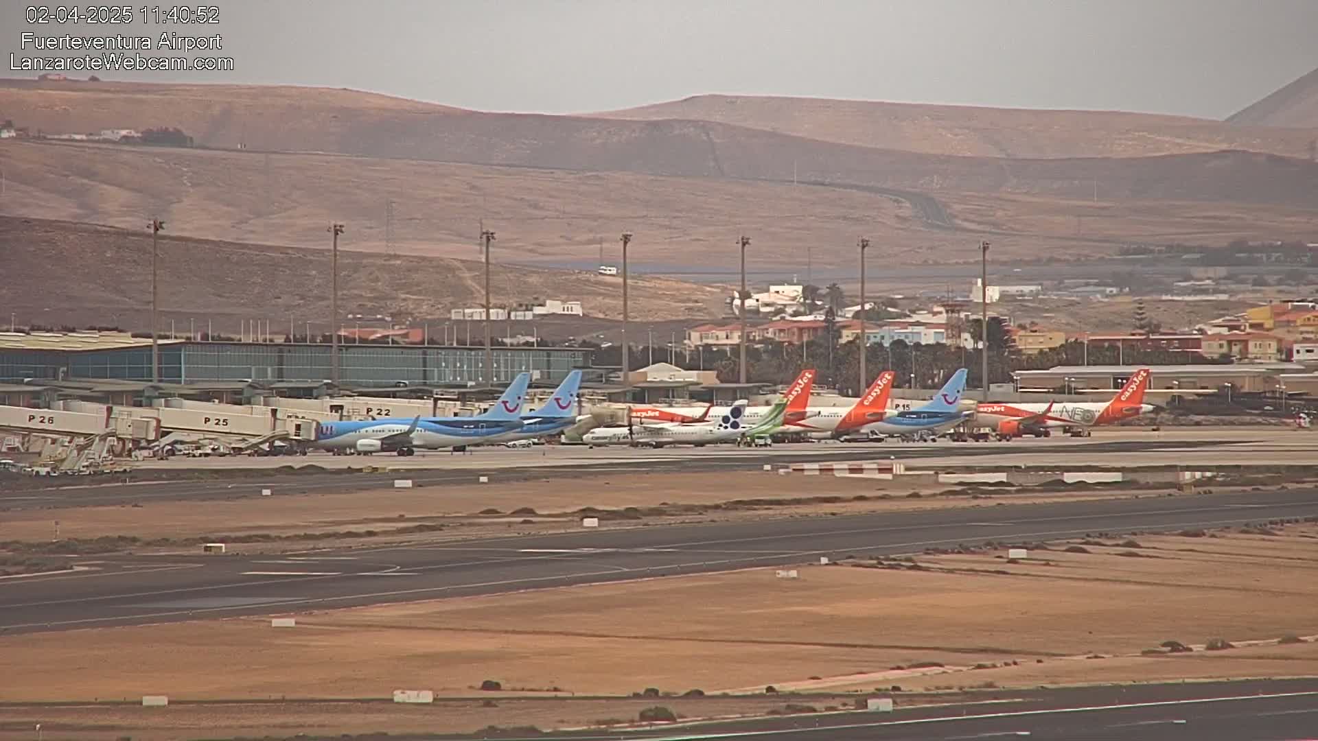 Several airplanes are parked at an airport tarmac under an overcast sky, with hills visible in the background.