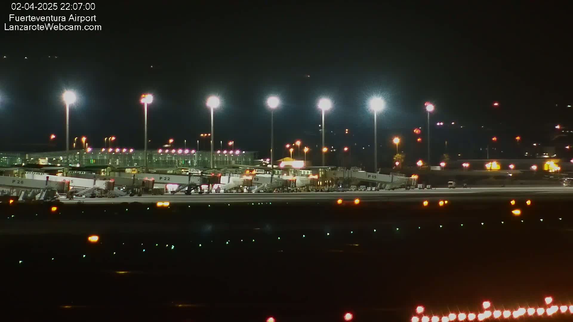 A brightly lit airport tarmac at night shows several airplanes connected to jet bridges.