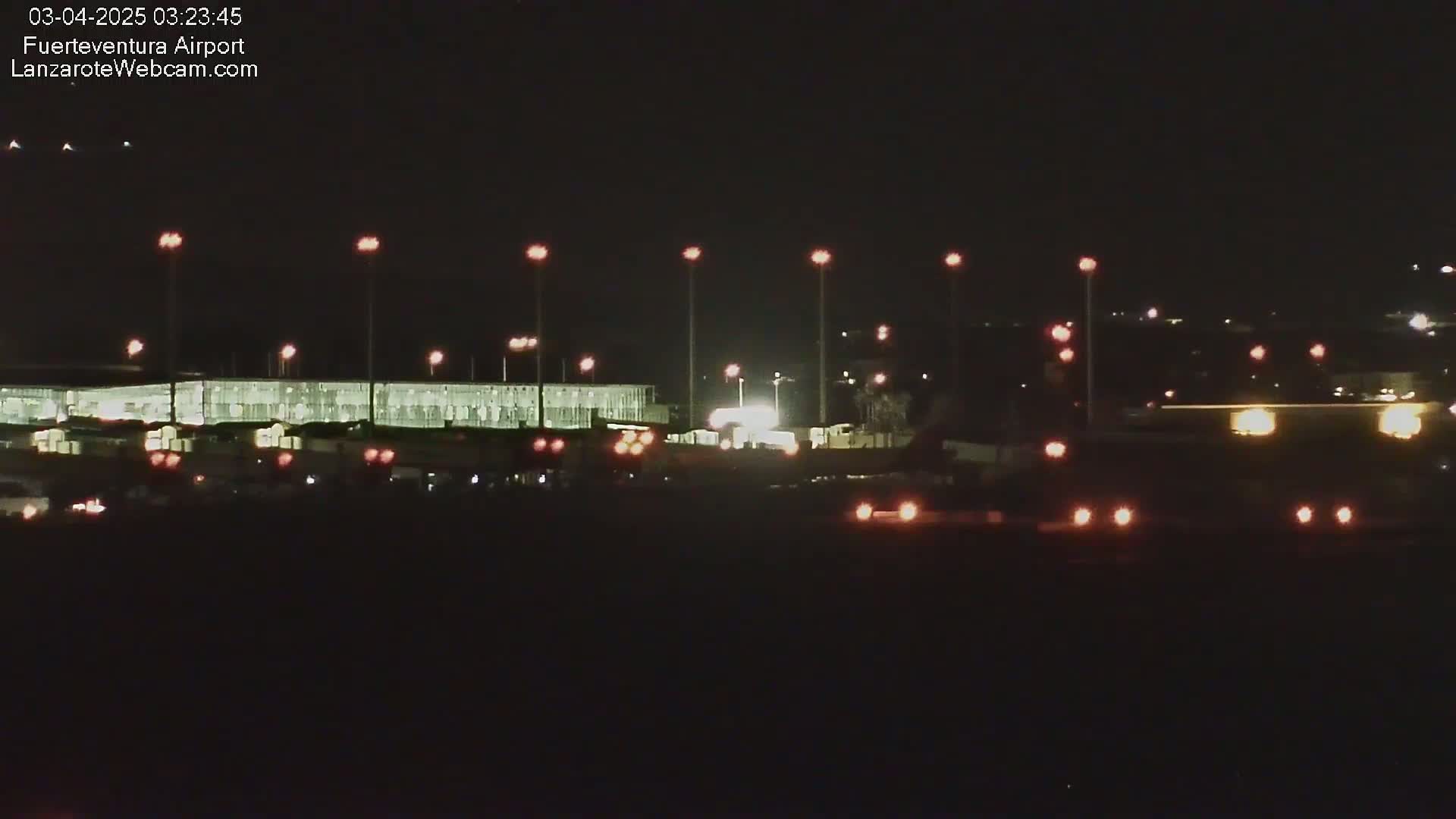 A nighttime view of an airport terminal building with numerous lights illuminating the tarmac and surrounding area.