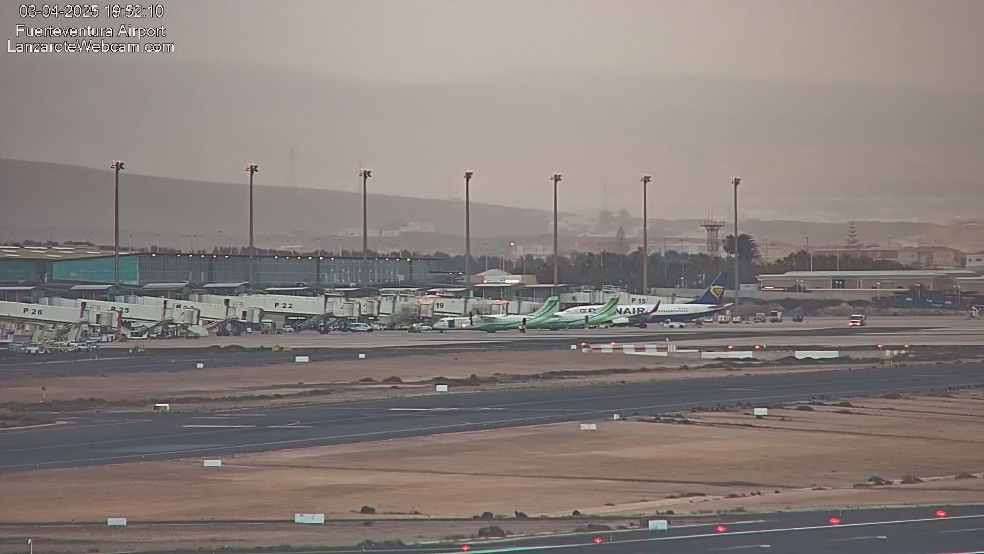 Several airplanes are parked at gates at an airport under hazy, dusty conditions.