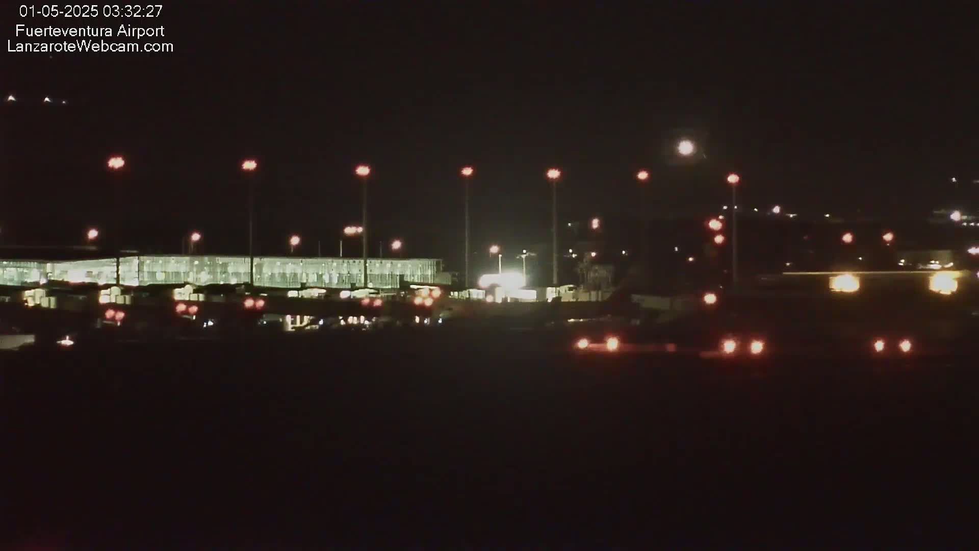 A brightly lit airport terminal is visible at night, illuminated by numerous lights against a dark sky.