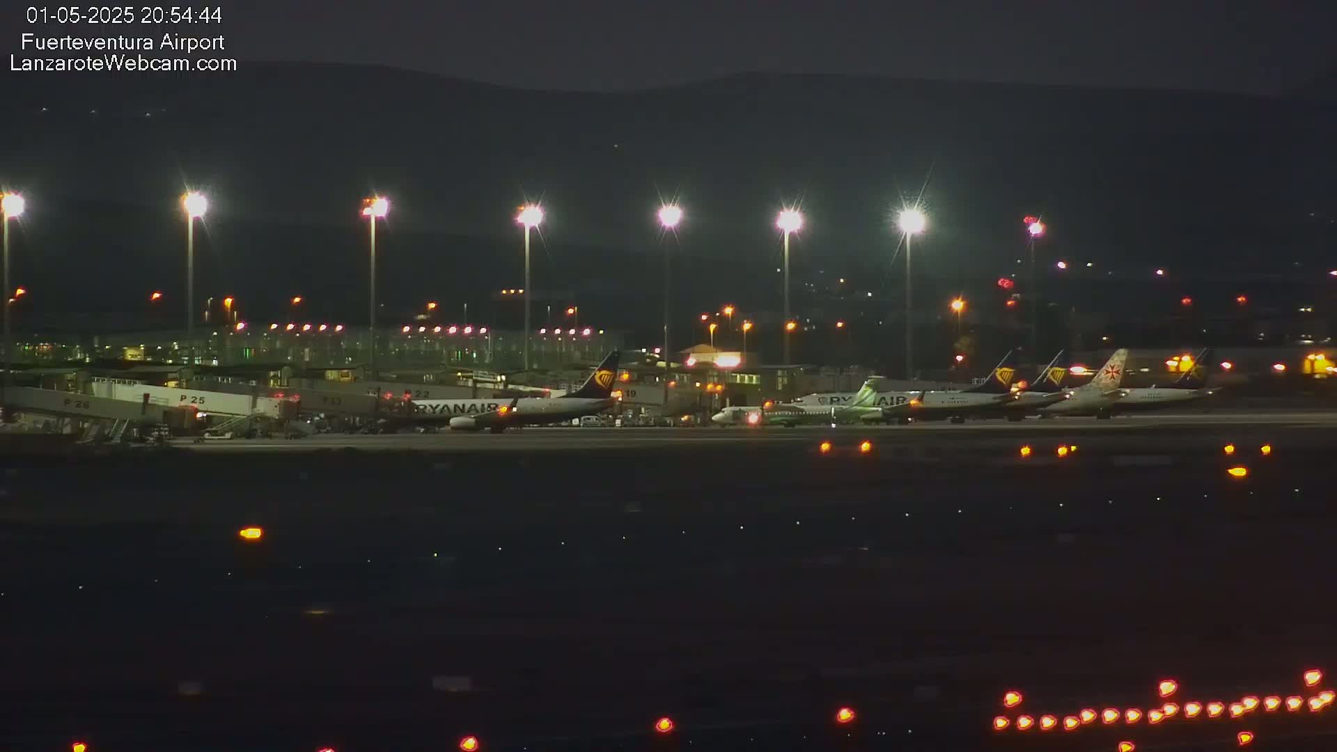 Several airplanes are parked at a brightly lit airport at night under a dark sky.