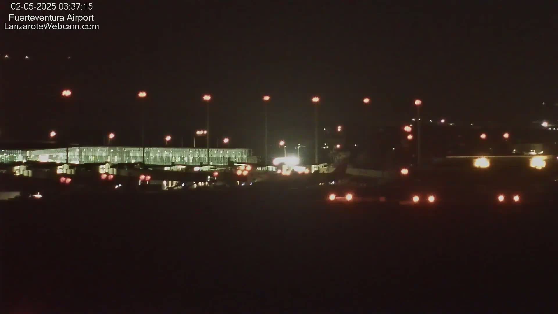 A brightly lit airport terminal at night is visible, with various vehicles and lights scattered across the tarmac.