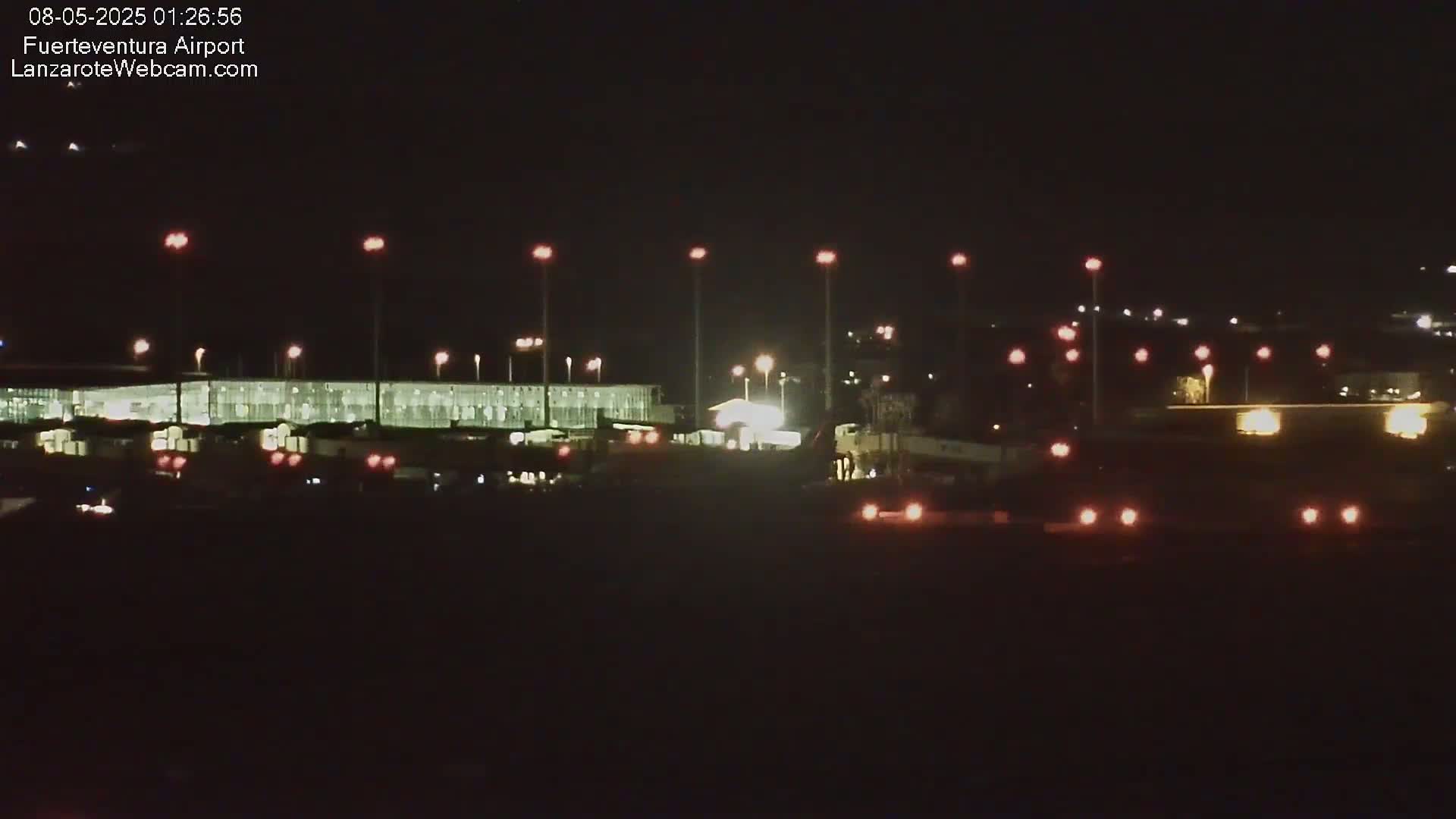 A brightly lit airport terminal at night is visible under a dark sky.