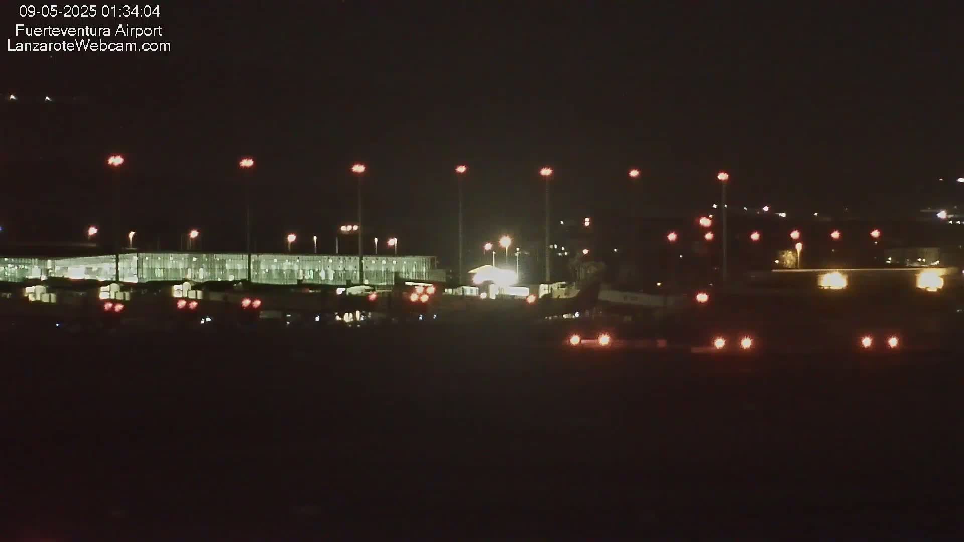 A brightly lit airport terminal at night is visible, with various lights illuminating the tarmac and surrounding area.