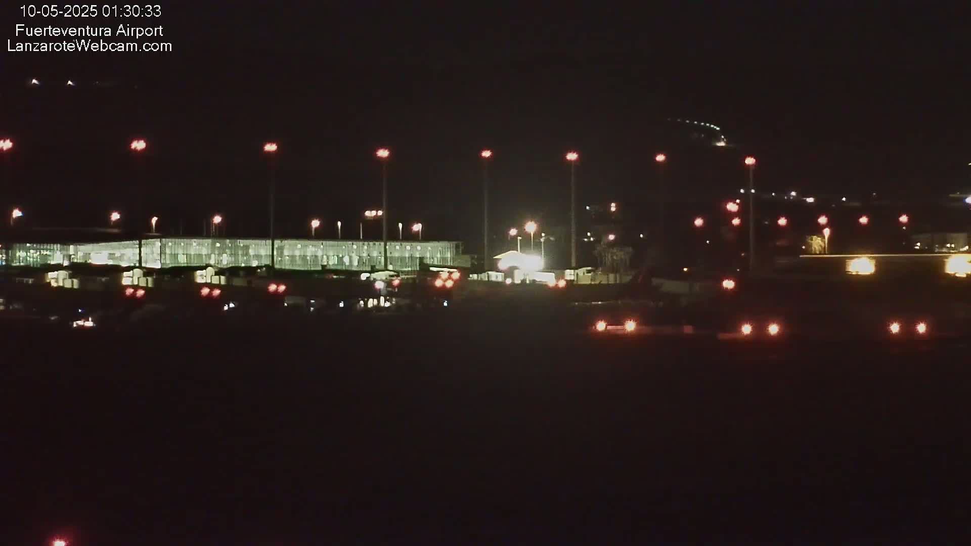 A nighttime view of an airport terminal building with various lights illuminating the tarmac and surrounding areas.
