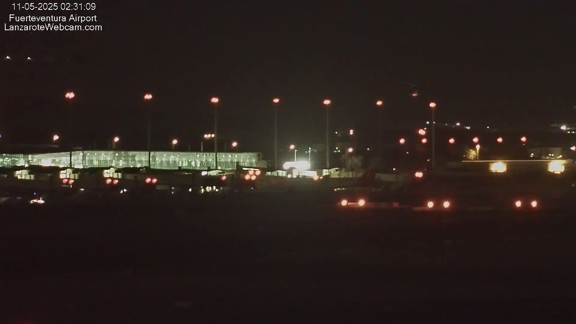 A nighttime view of an airport terminal building and tarmac illuminated by numerous lights.