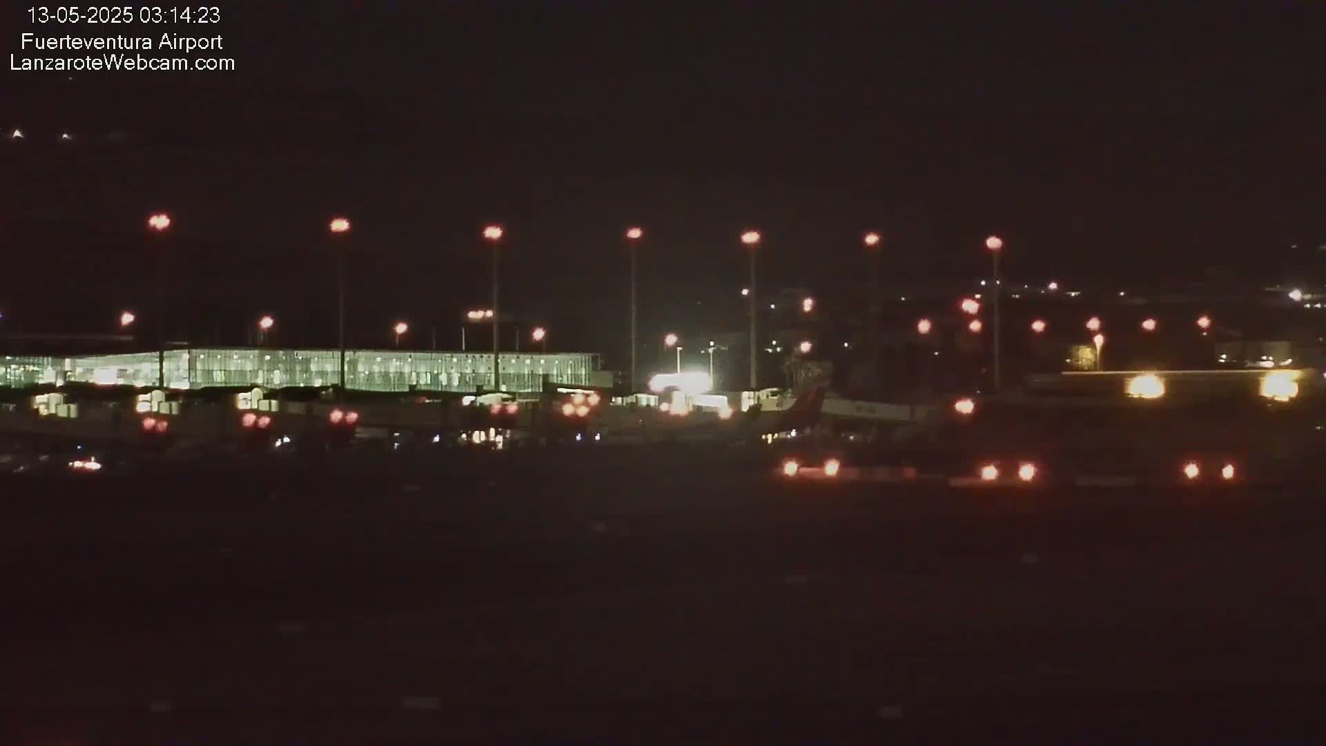 A nighttime long shot of an airport terminal building and tarmac, illuminated by numerous lights.