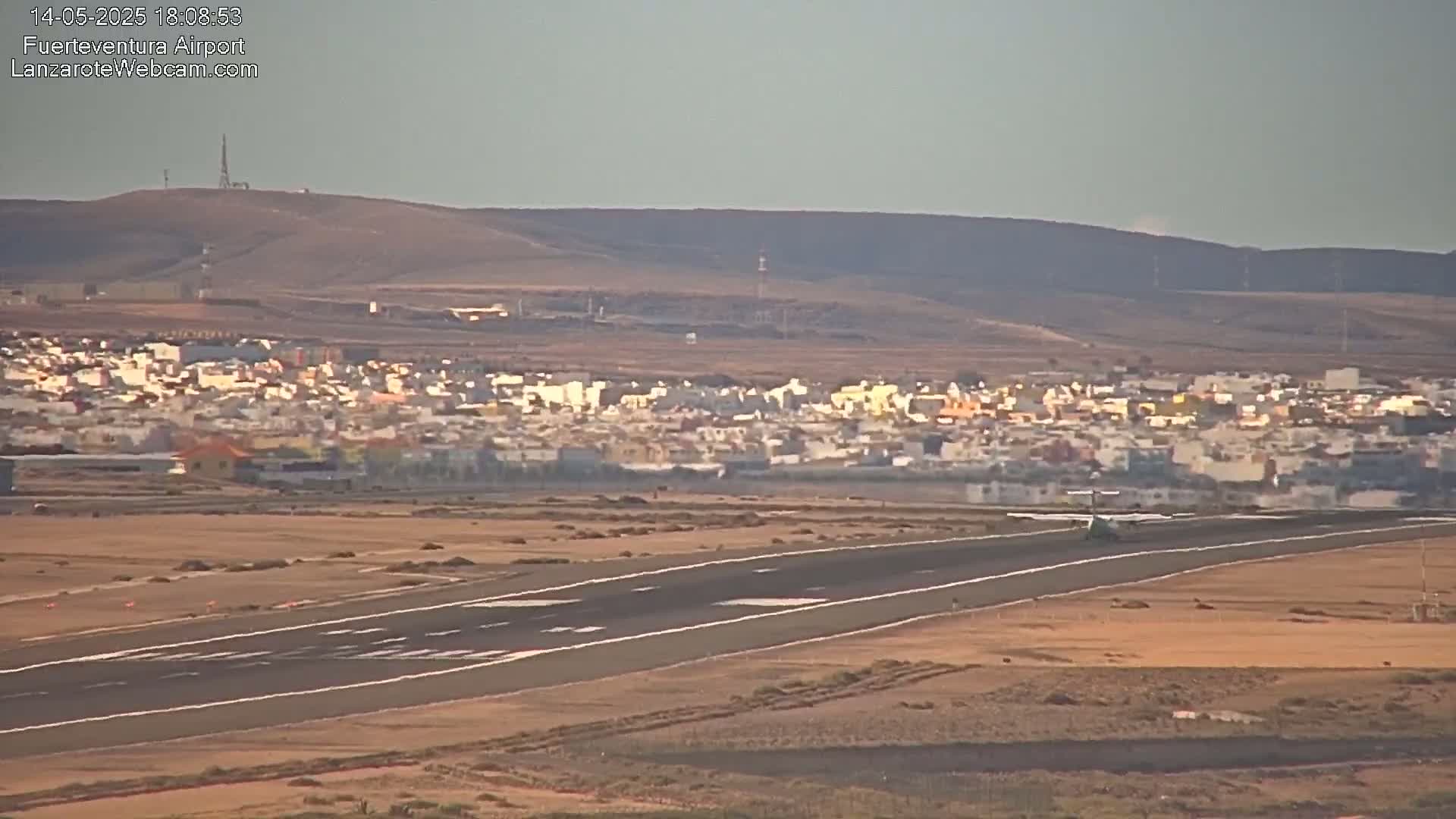 A small airplane taxis on a runway near a town under a hazy sky.