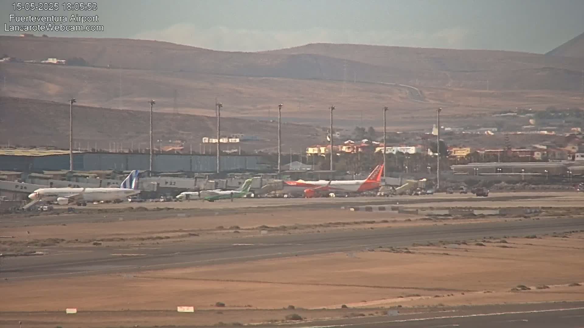 Several airplanes are parked on an airport tarmac under hazy conditions, with buildings and hills visible in the background.