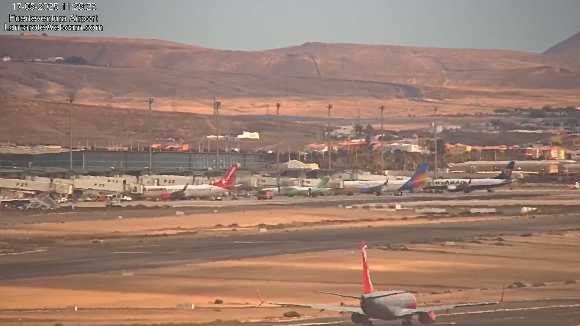 Several airplanes are parked at an airport tarmac under a mostly clear sky, with one airplane taxiing on the runway.