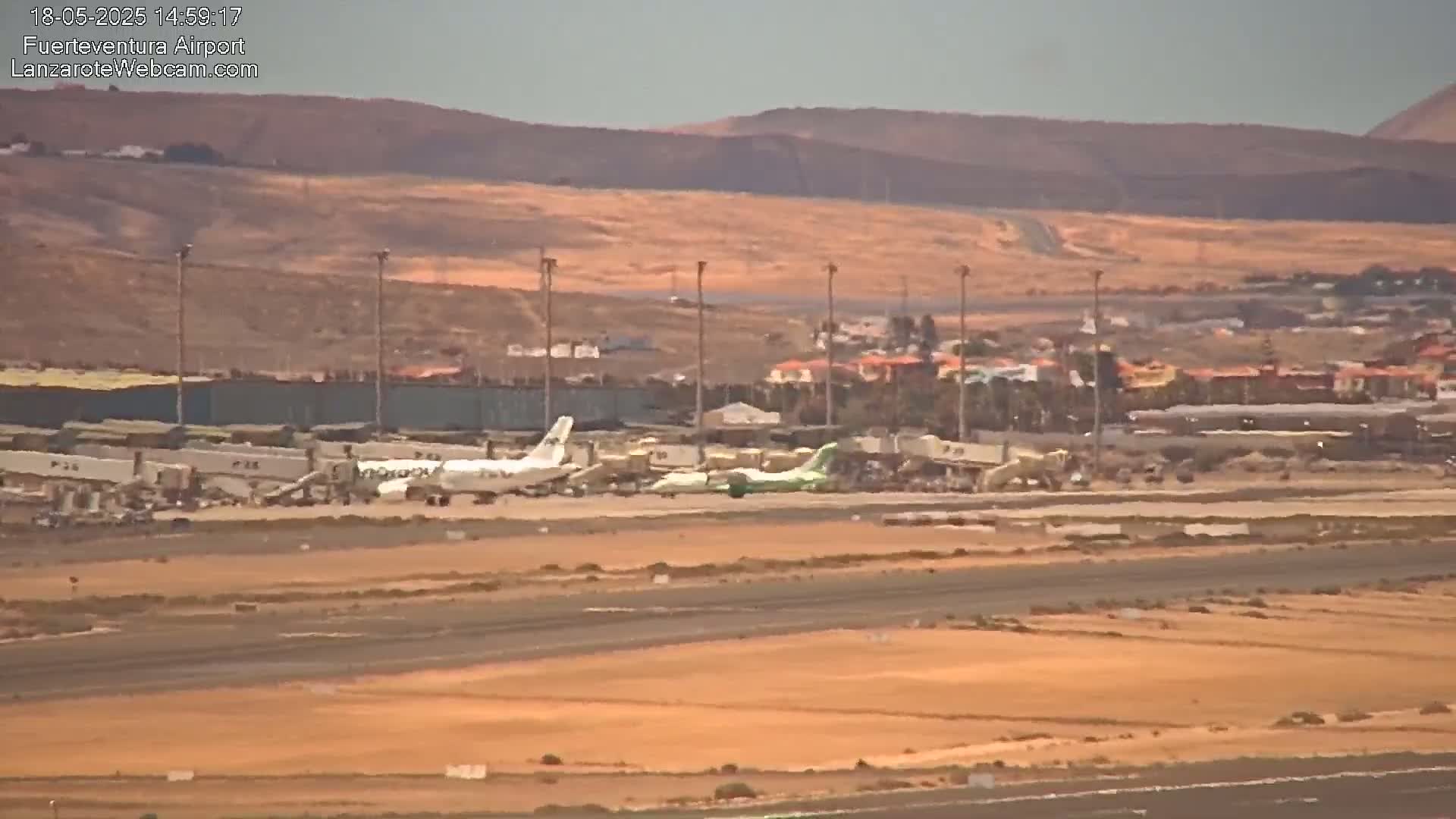 Several airplanes are parked at an airport on a sunny day with tan-colored hills in the background.