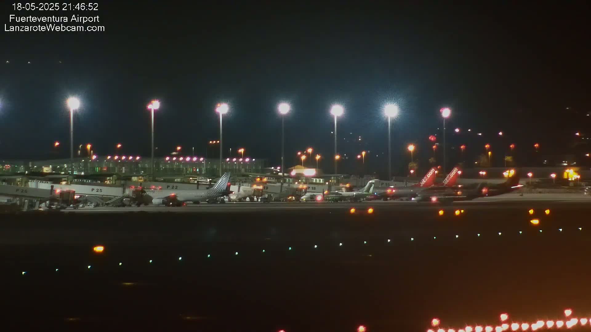 Several airplanes are parked at night at a brightly lit airport tarmac.