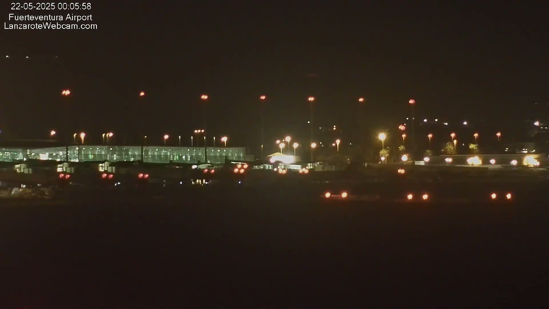 A nighttime long shot of an airport terminal and tarmac, illuminated by numerous lights under a clear, dark sky.
