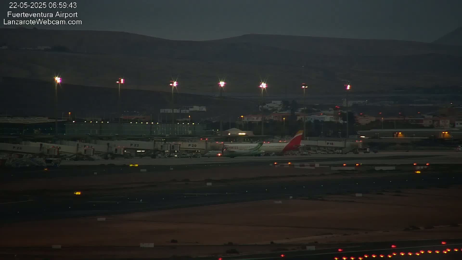 A passenger airplane sits on a tarmac at an airport at dusk under a dark sky.