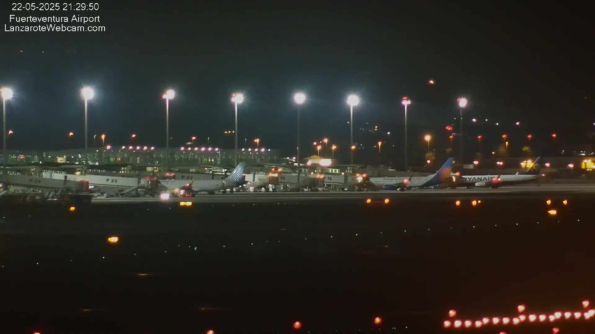 Several airplanes are parked at a brightly lit airport at night.