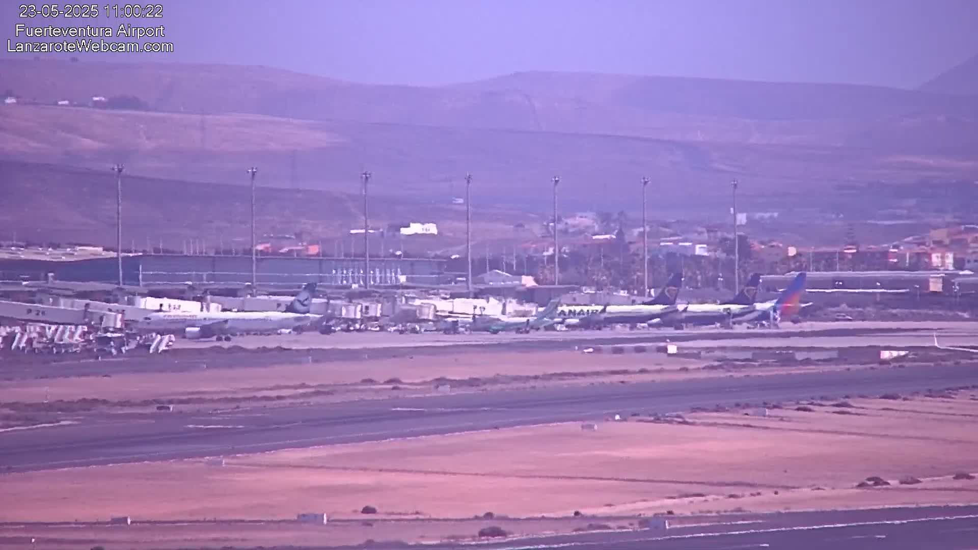 Several airplanes are parked at an airport on a hazy day with a mountainous backdrop.