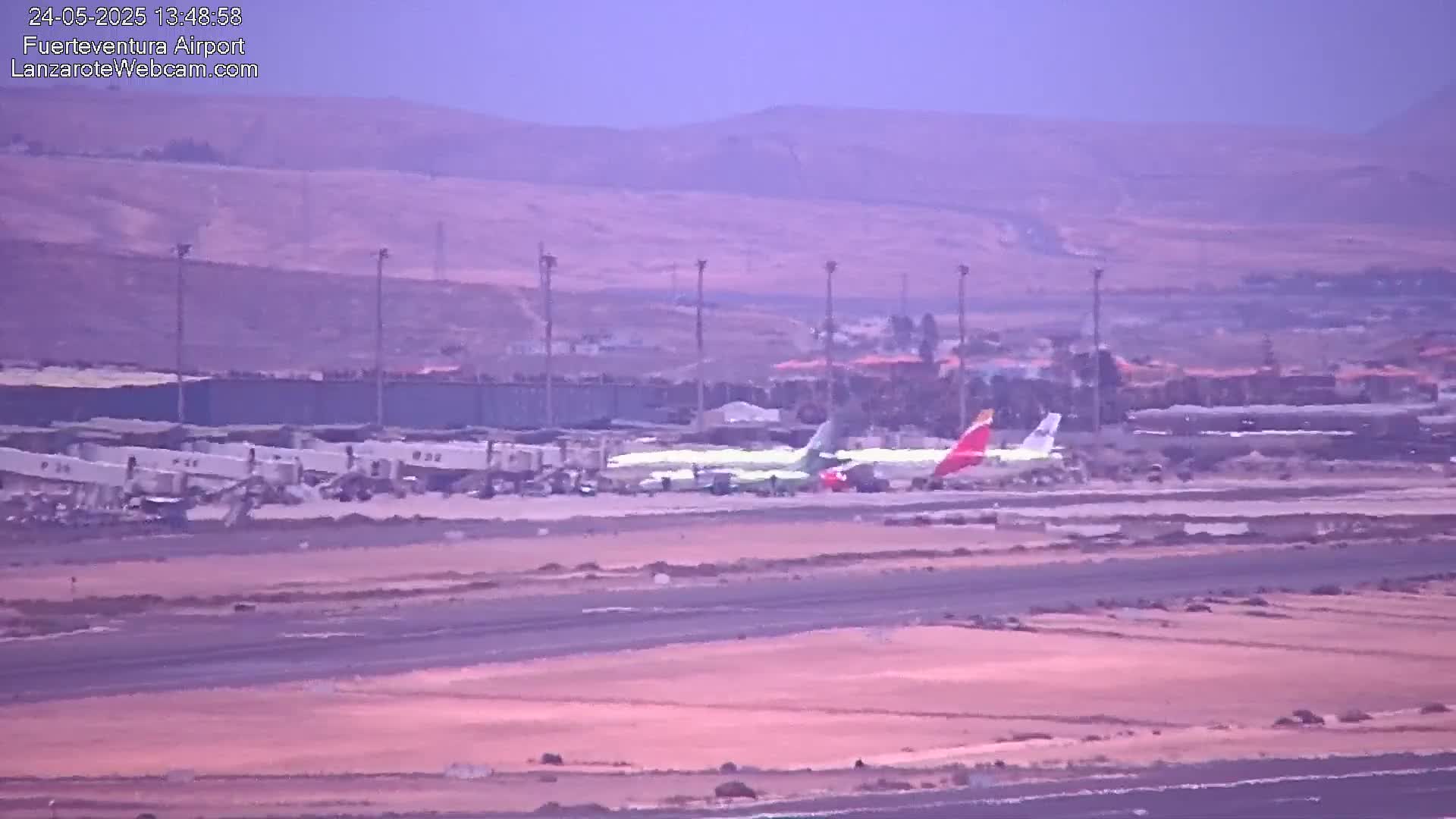 Two airplanes are parked on an airport tarmac under hazy skies, with a distant view of brown hills in the background.