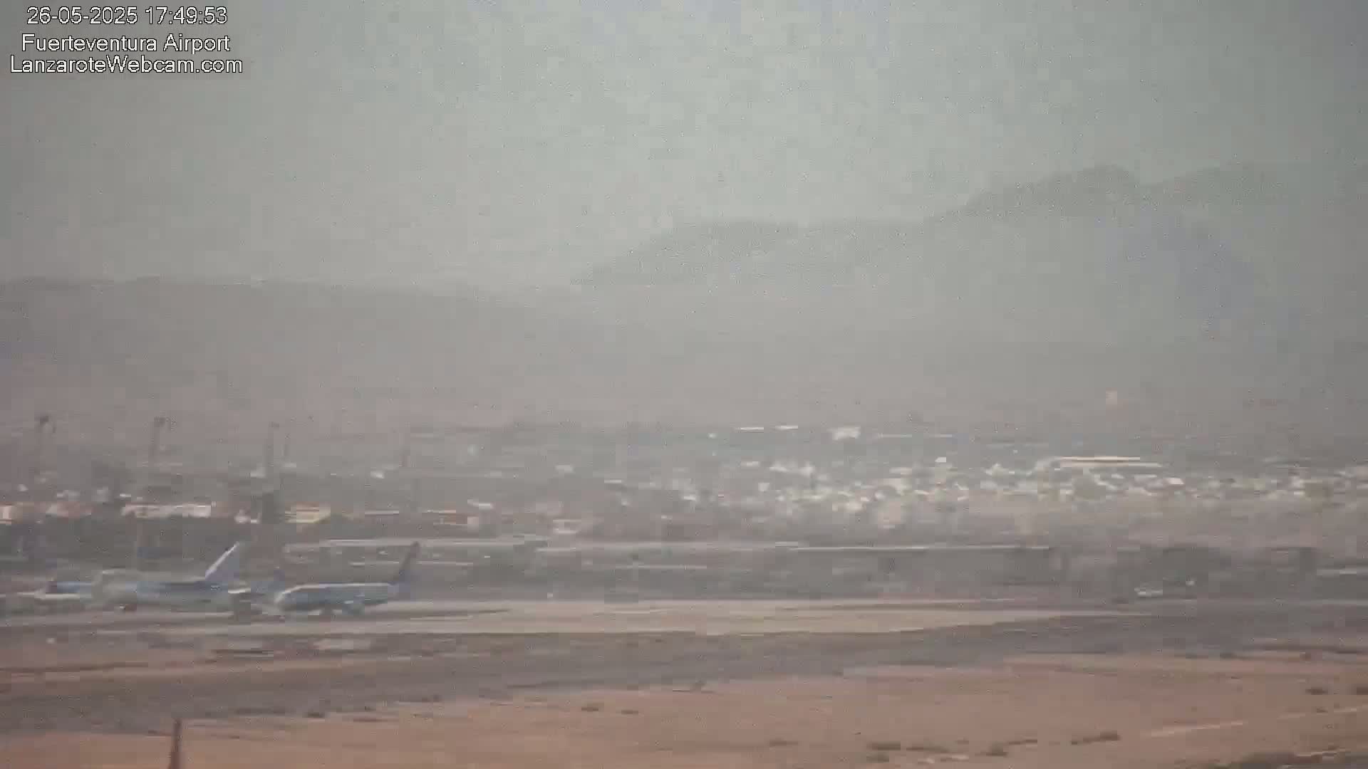 Two airplanes are taxiing on a hazy airport runway with distant, dusty mountains visible in the background.