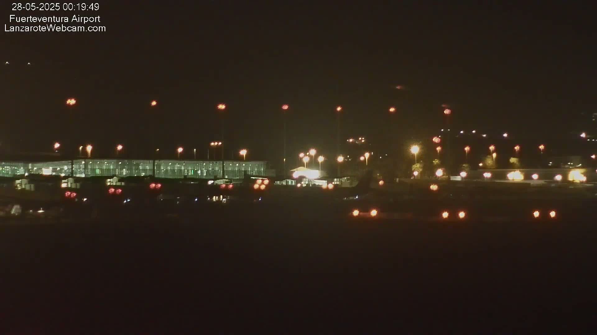 A nighttime view of an airport terminal building illuminated by numerous lights, under a clear, dark sky.